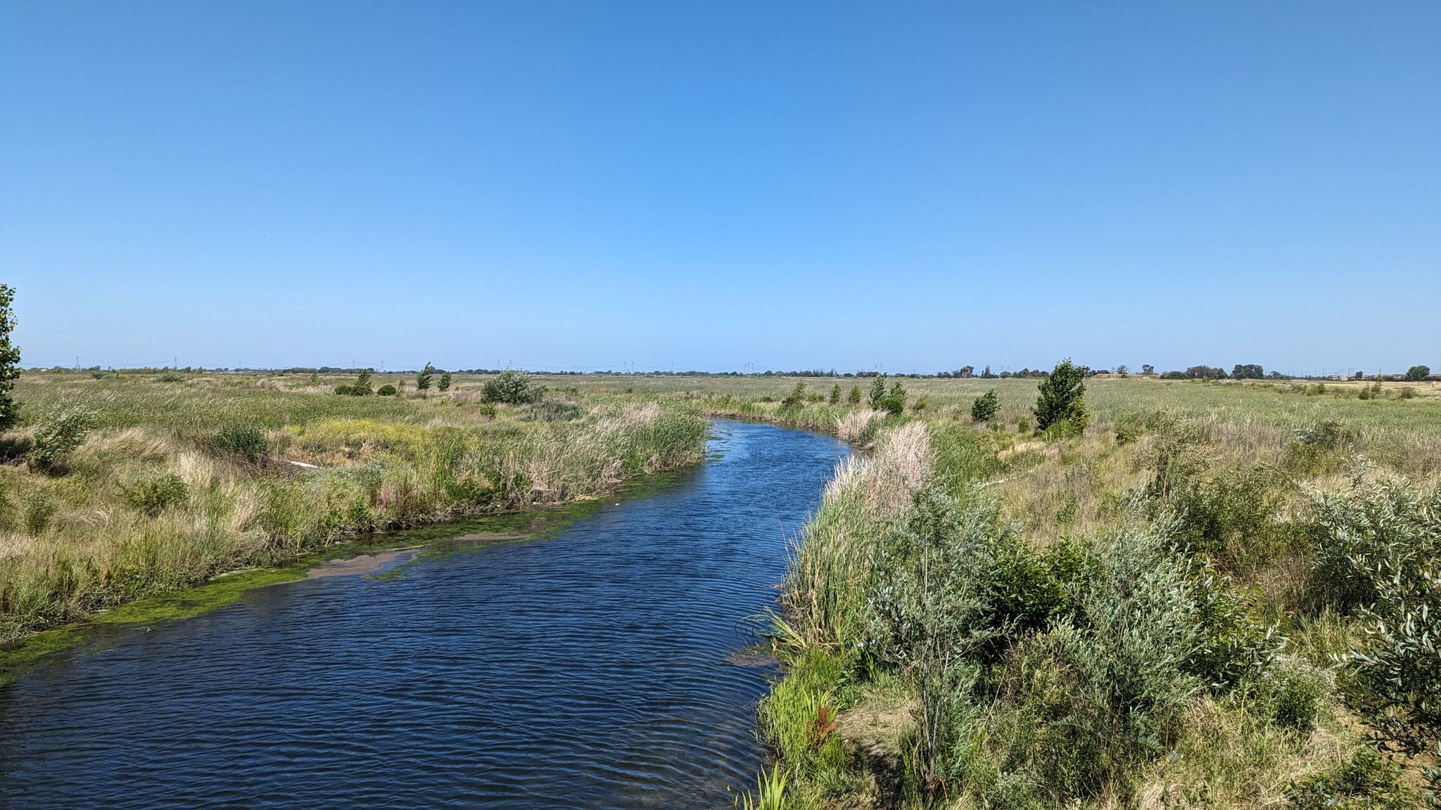 A winding river flows through vast grassy plains under a bright blue sky. - Marsh Creek Regional Trail