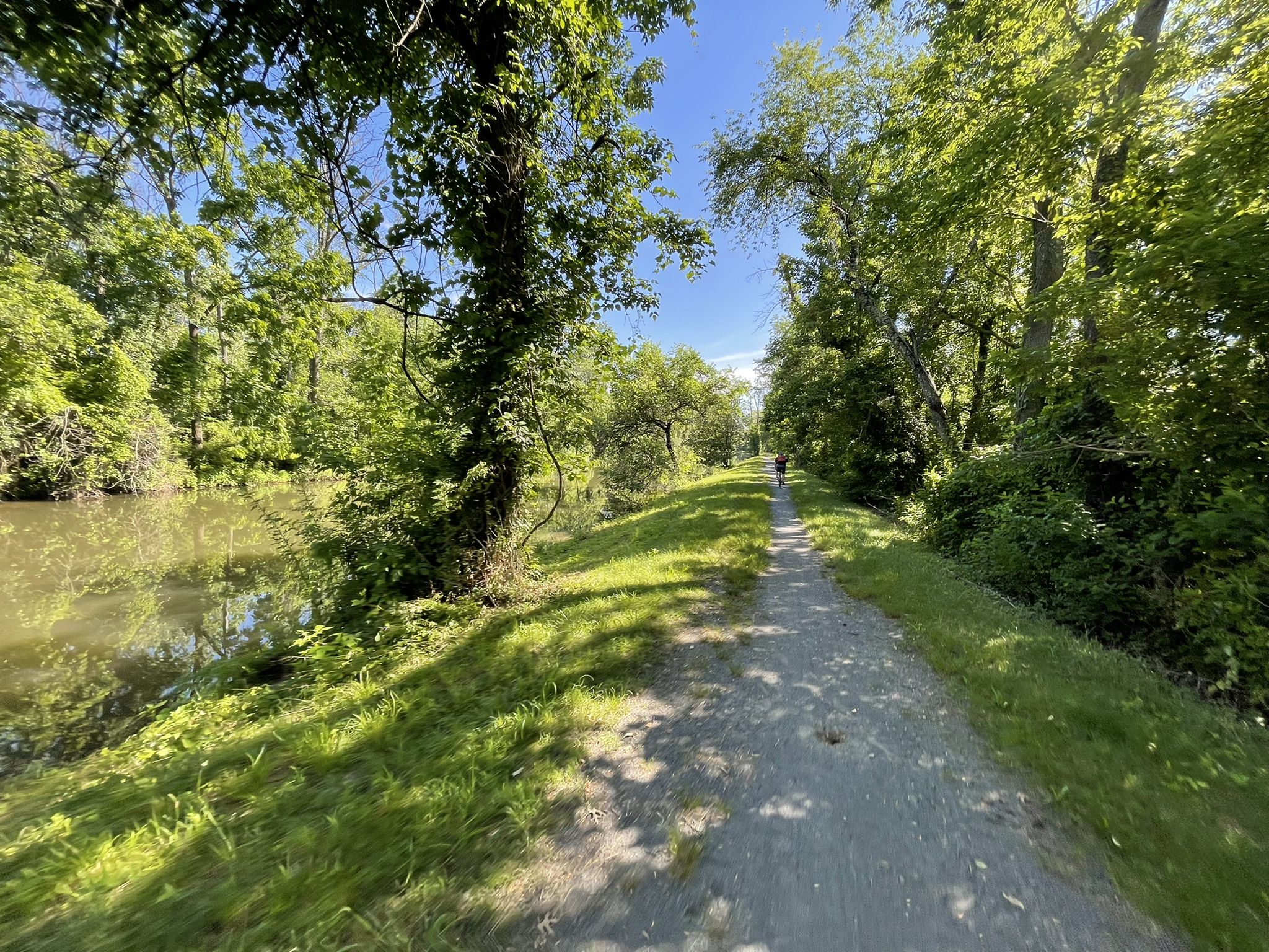 Sunny dirt path next to a canal, with a person walking ahead. - D&R Canal and Johnson Trolley Trail Loop