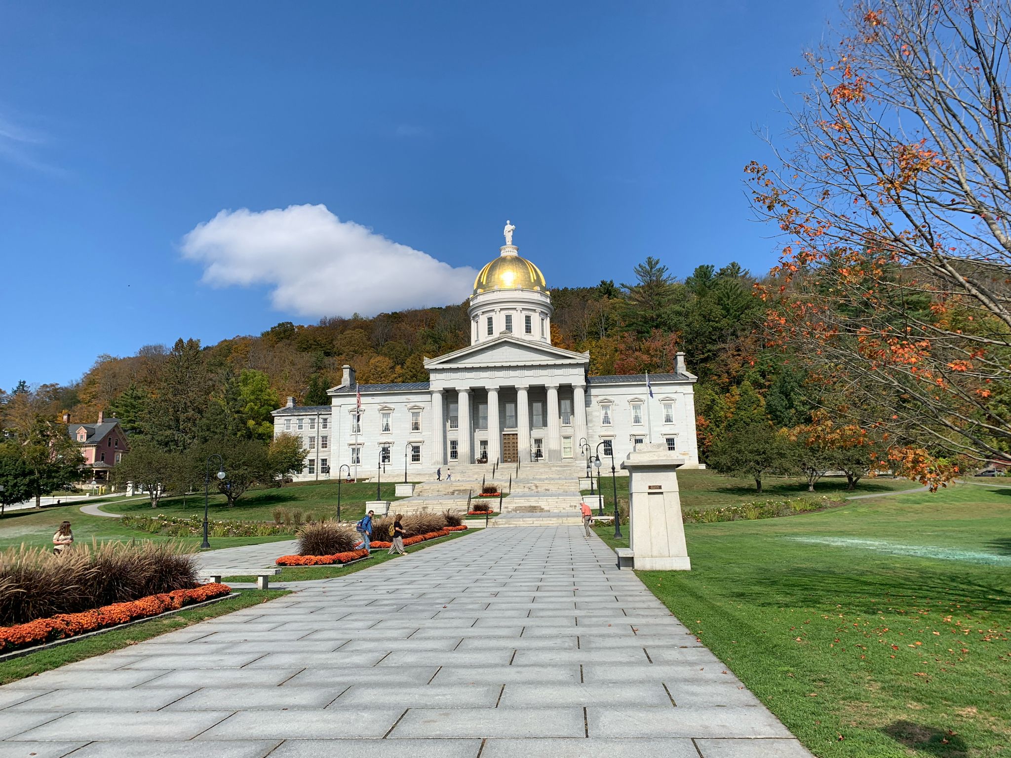 Grand white building with golden dome, autumn trees, and sunny blue sky. - Winooski West Path – Small Falls loop from Montpelier