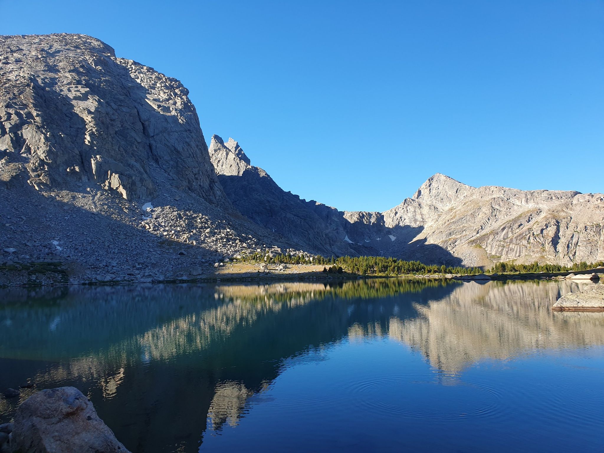 Calm lake perfectly reflects rugged mountains and a clear blue sky. - Cirque of the Towers – Lonesome Lake loop from Wolfs Head