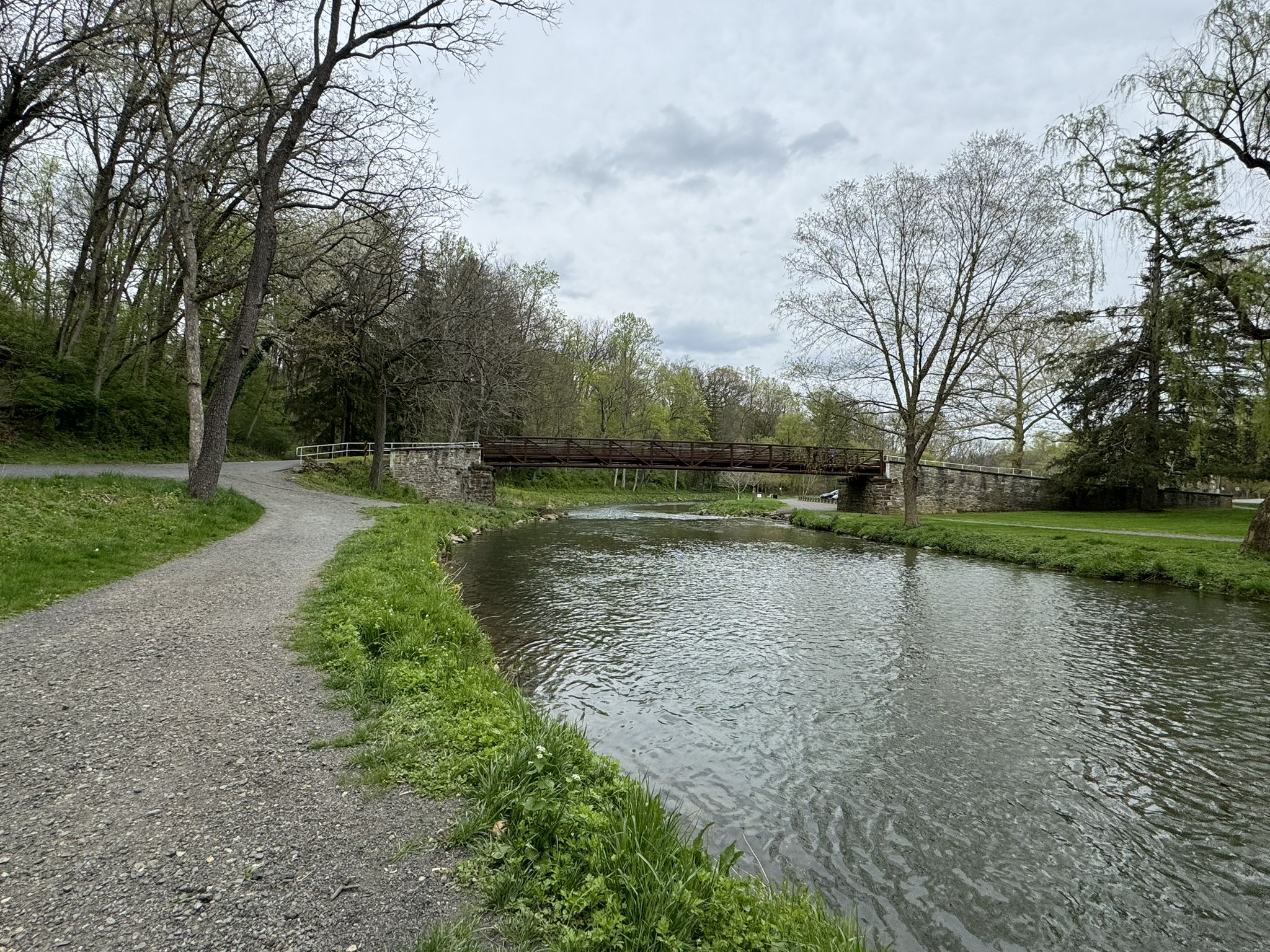A gravel path runs alongside a river with a distant bridge on an overcast day. - Bogert Covered Bridge loop from Allentown Queen City Municipal Airport (KXLL)