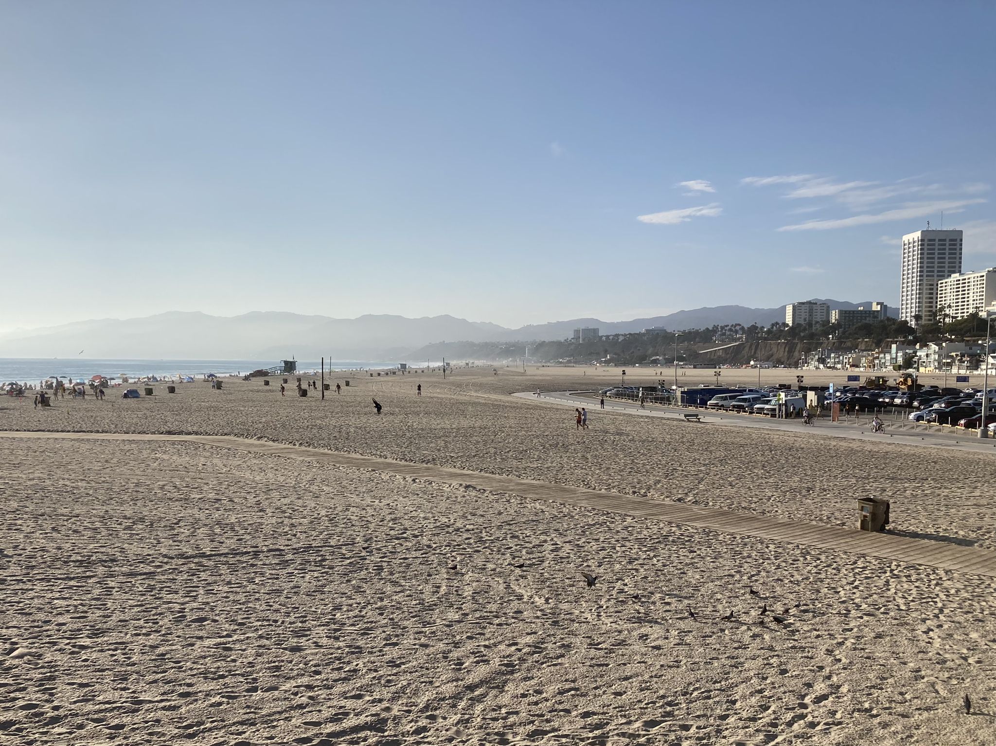 Wide sandy beach with scattered people, distant city buildings, and mountains. - Venice Beach Boardwalk out and back & Santa Monica