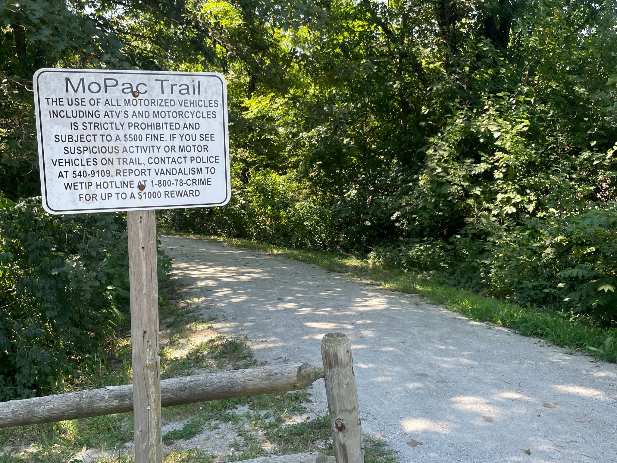 A white sign on a wooden post next to a gravel path and trees. - Rock Island Lake loop from Lee's Summit
