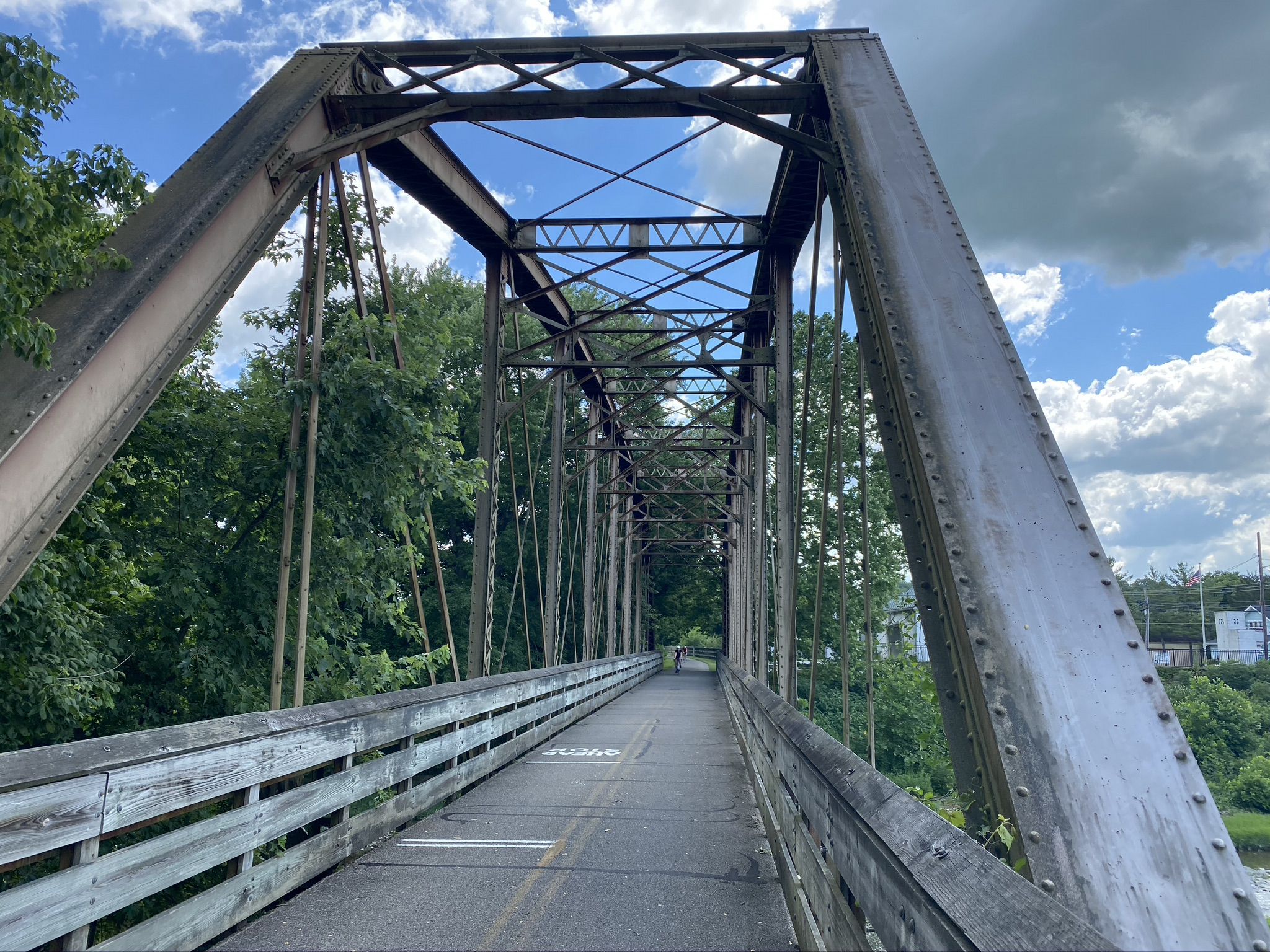 Long metal truss bridge with a paved path, person in distance, cloudy sky. - Little Miami Scenic Trail