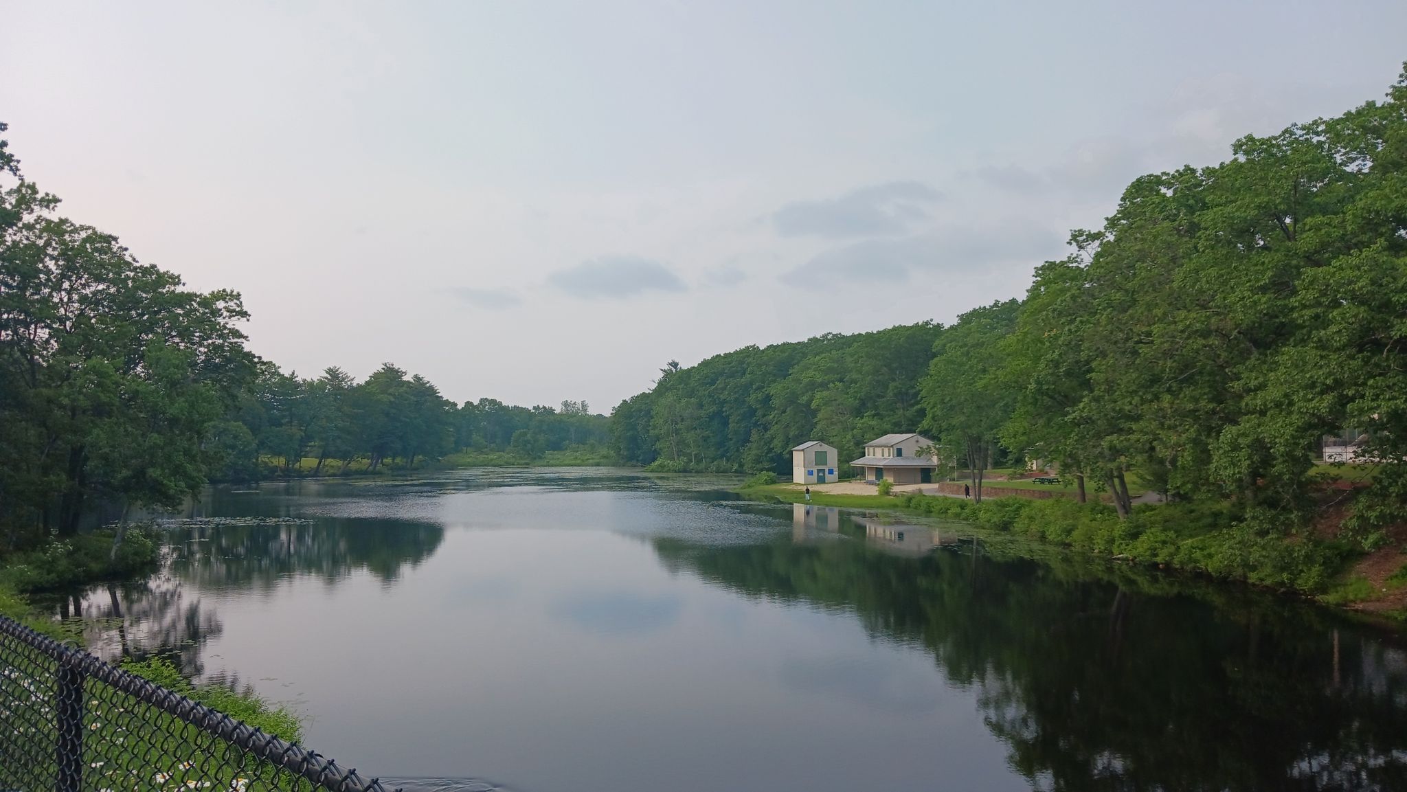 Calm river reflecting overcast sky, flanked by dense green trees and houses. - Londonderry Rail Trail – Hood Park loop from Manchester–Boston Regional Airport
