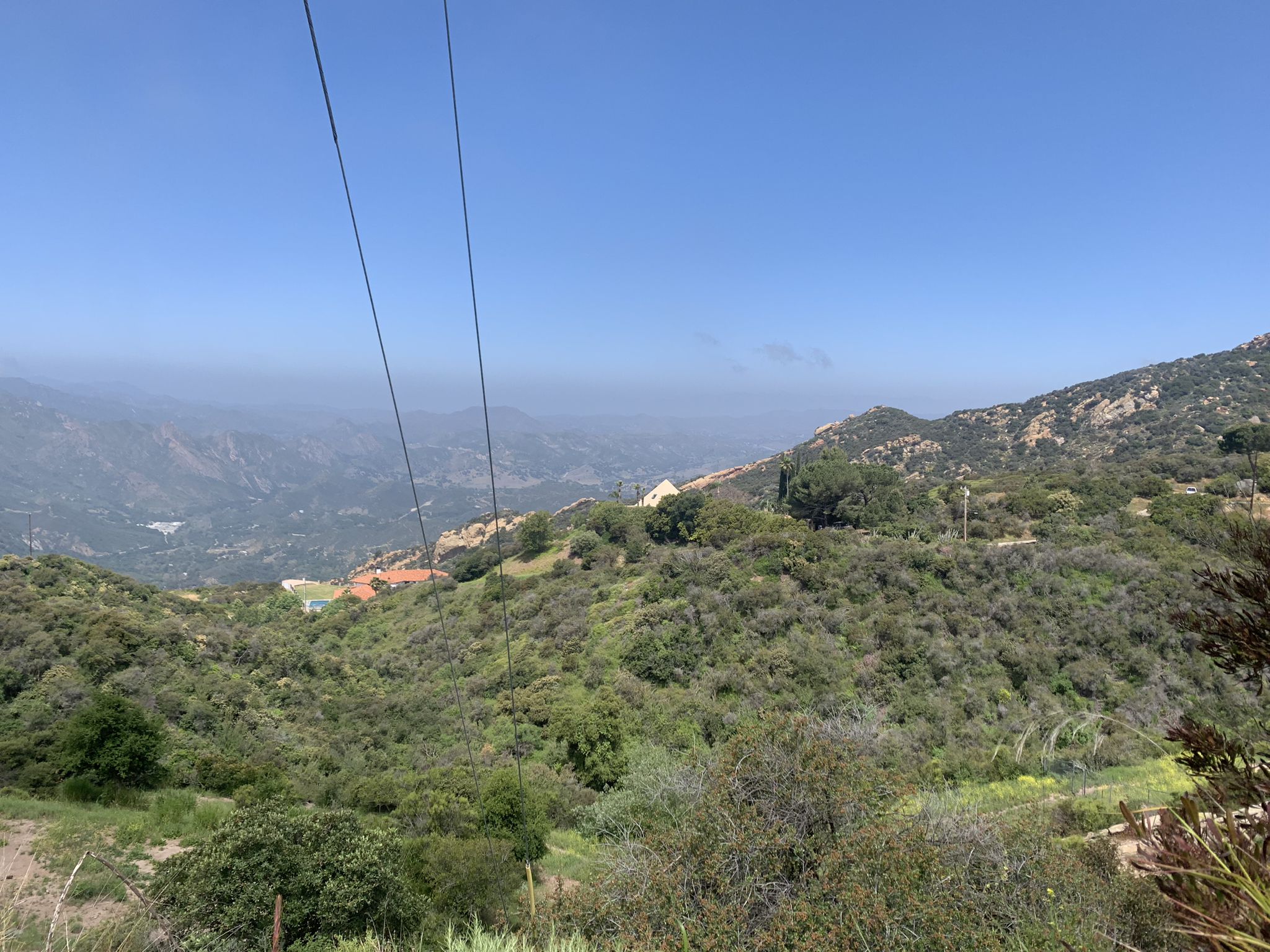 Sunny view of green, brush-covered mountains with power lines and hazy distant hills. - MRCA Open Space loop from Cold Creek Canyon Preserve