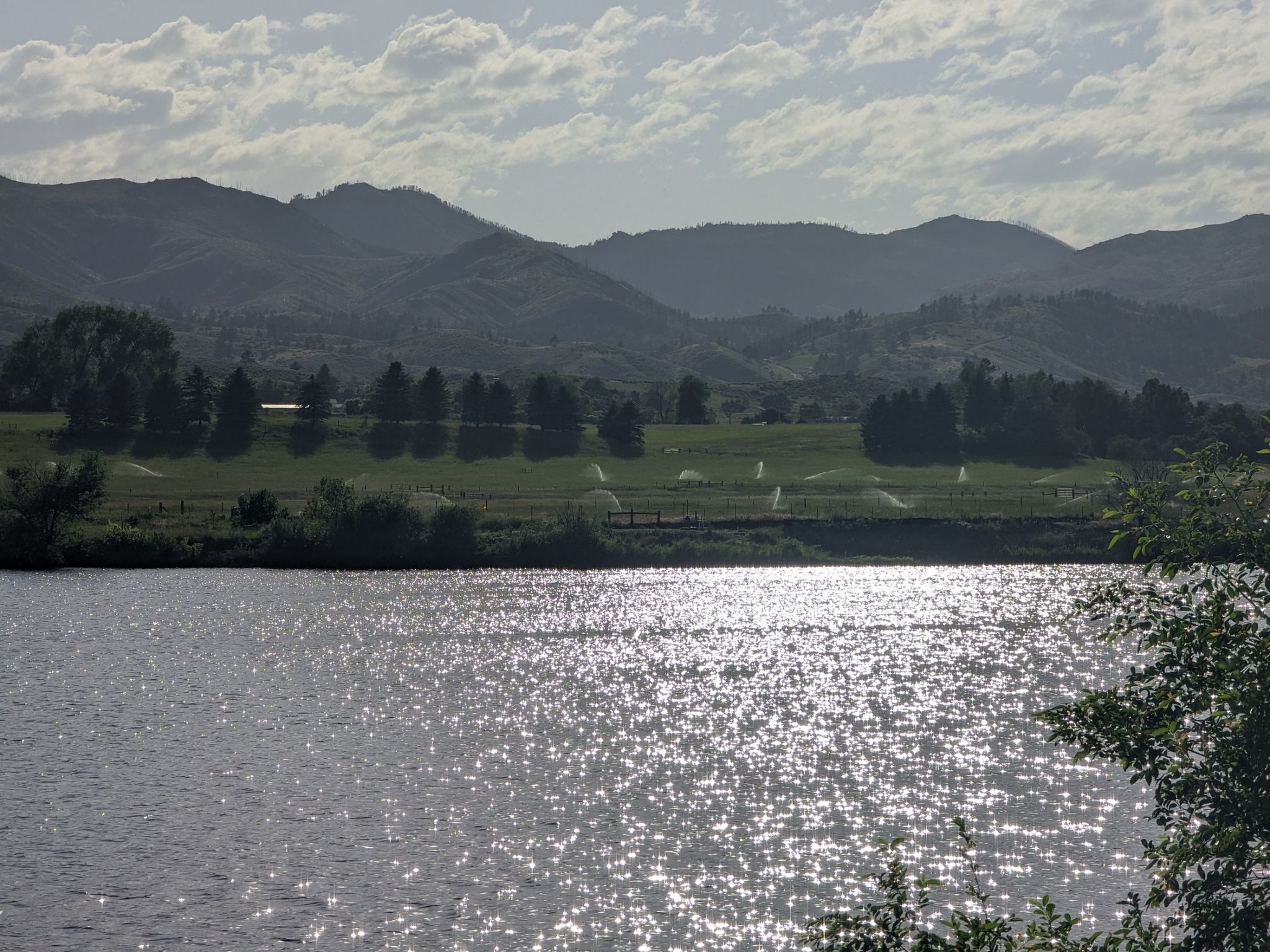 Sun glinting on a lake with distant green fields and mountains. - Poudre River Trail