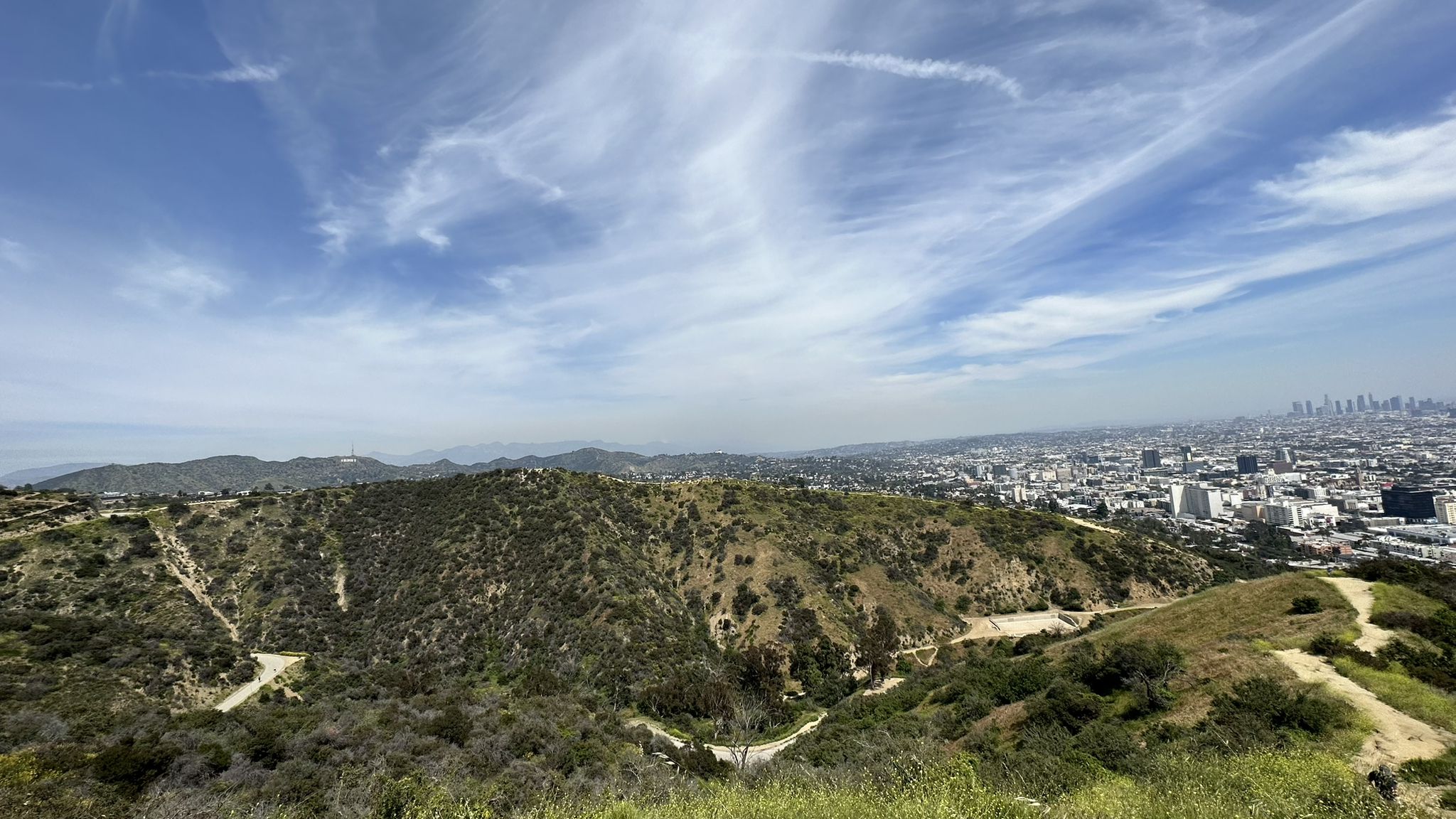 Expansive view of green hills and a distant city under a partly cloudy sky. - Inspiration Point – Runyon Canyon Park