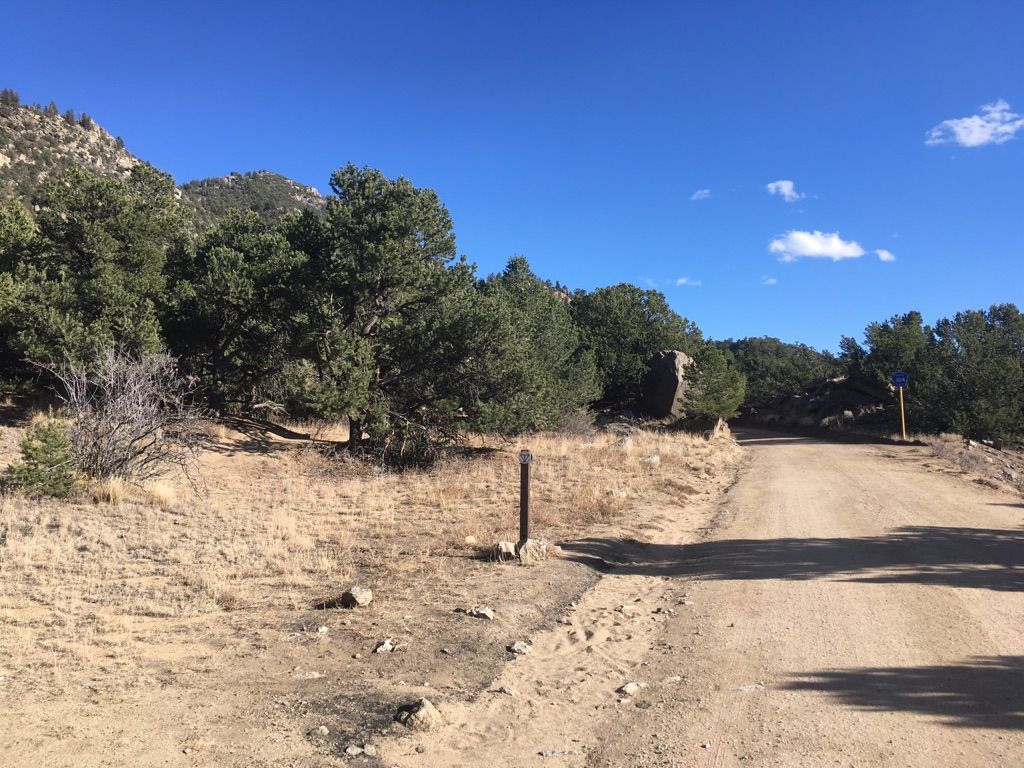 A dirt road winds through arid hills with scattered trees under a clear sky. - North Broken Boyfriend Loop