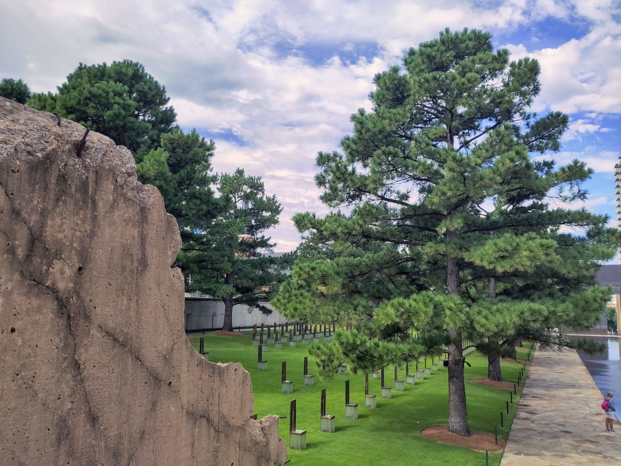 Large pine trees and memorial chairs on green grass under cloudy sky. - Lake Hefner Lighthouse – Bert Cooper Trails loop from Harvest Hills Church