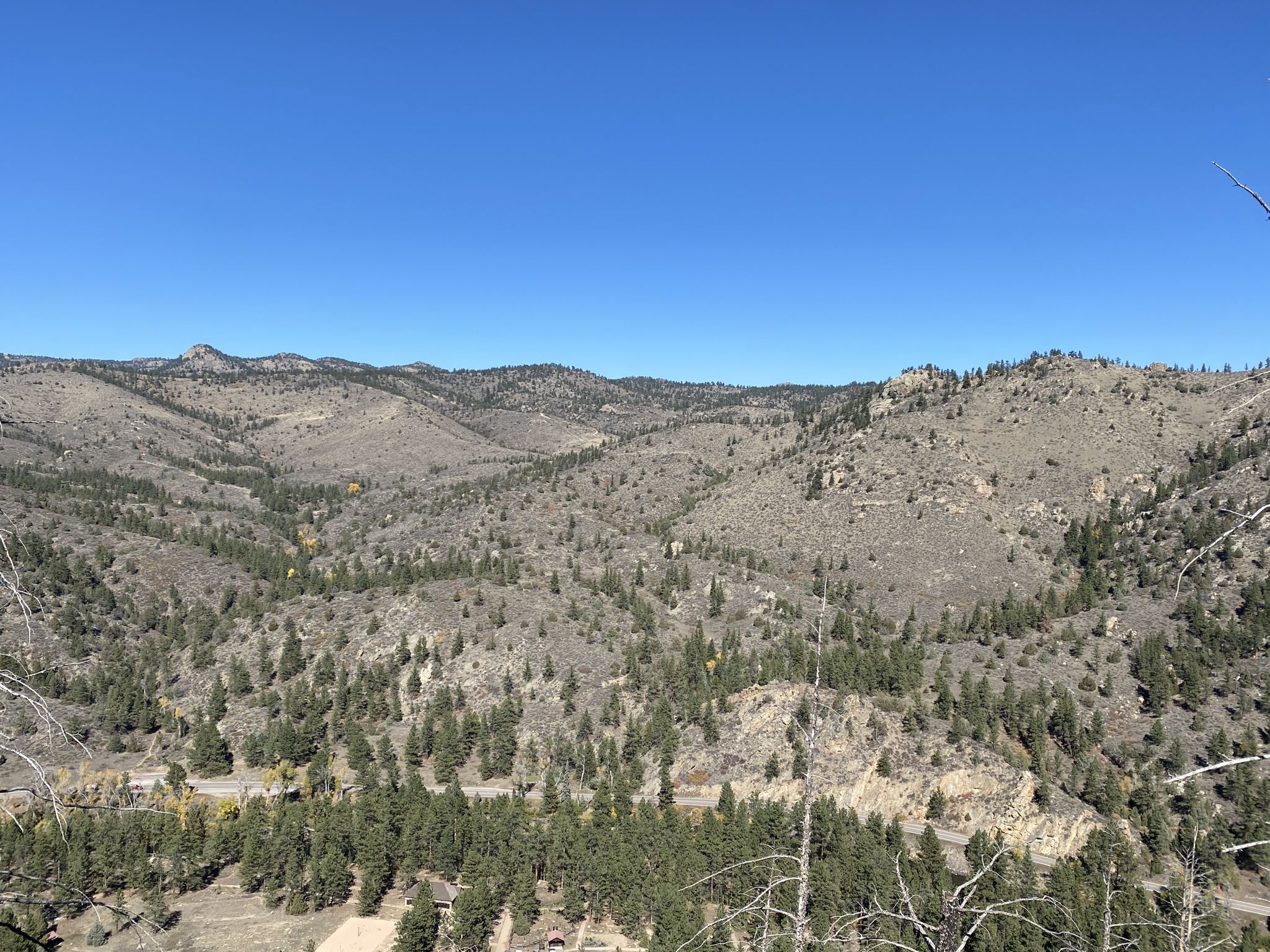 Wide sunny view of rolling mountains with scattered trees and a valley road. - Kreutzer Nature Trail