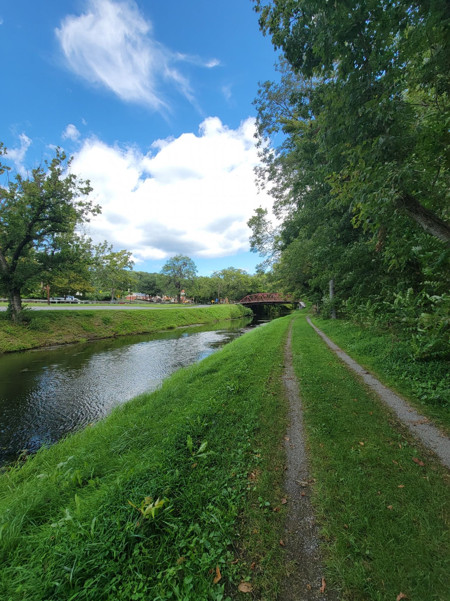 A dirt path runs beside a canal with a red bridge in distance. - Chesapeake and Ohio Canal Towpath