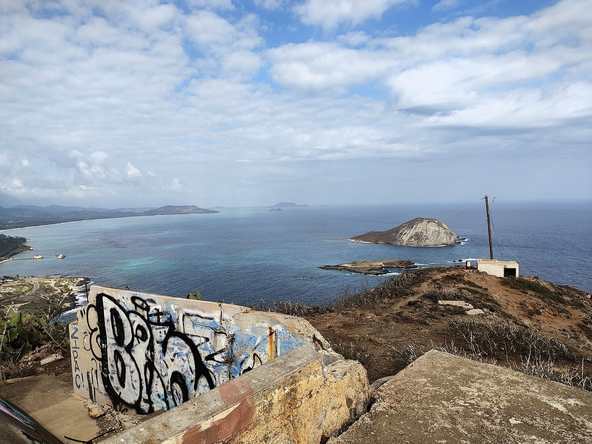 Coastal view with ocean, islands, and graffiti-covered concrete structure under cloudy sky. - Makapu'u Point Trail (Makapu'u Head and Makapu'u lighthouse) – Kaiwi State Scenic Shoreline