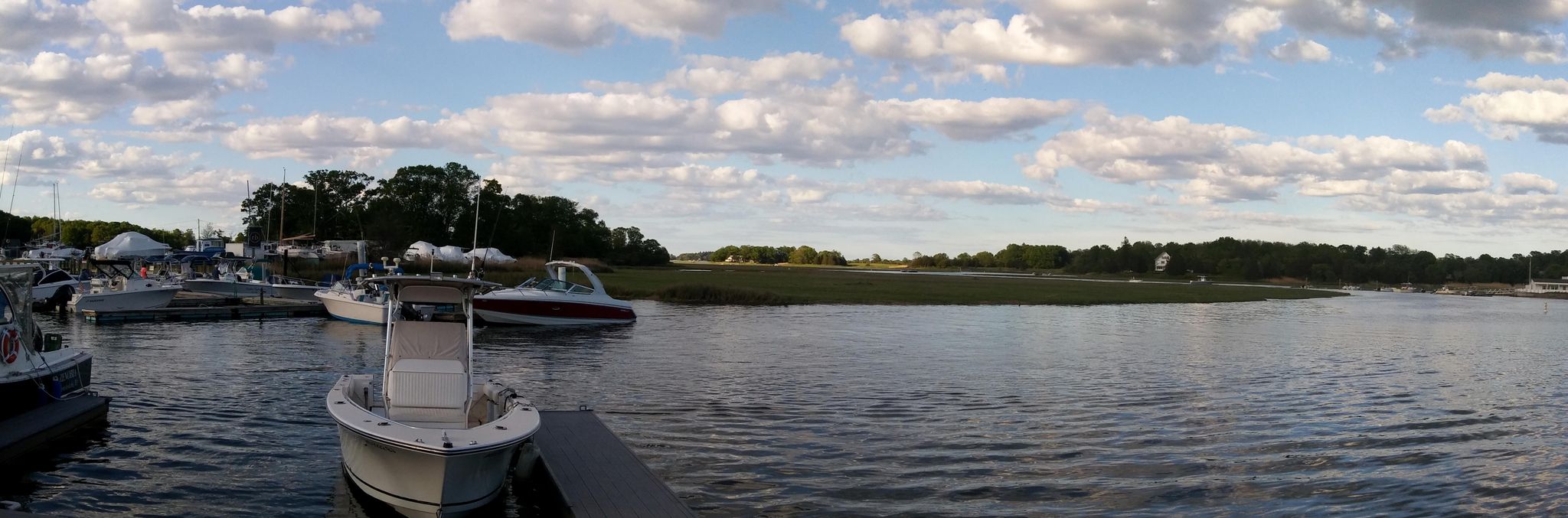 Boats docked in a calm marina, with marshland and cloudy sky. - Essex River loop from Chebacco Lake