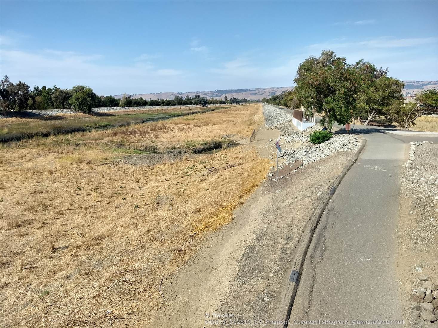 Sunny view of a dry field, paved path, and distant green trees. - Alameda Creek Trail Loop