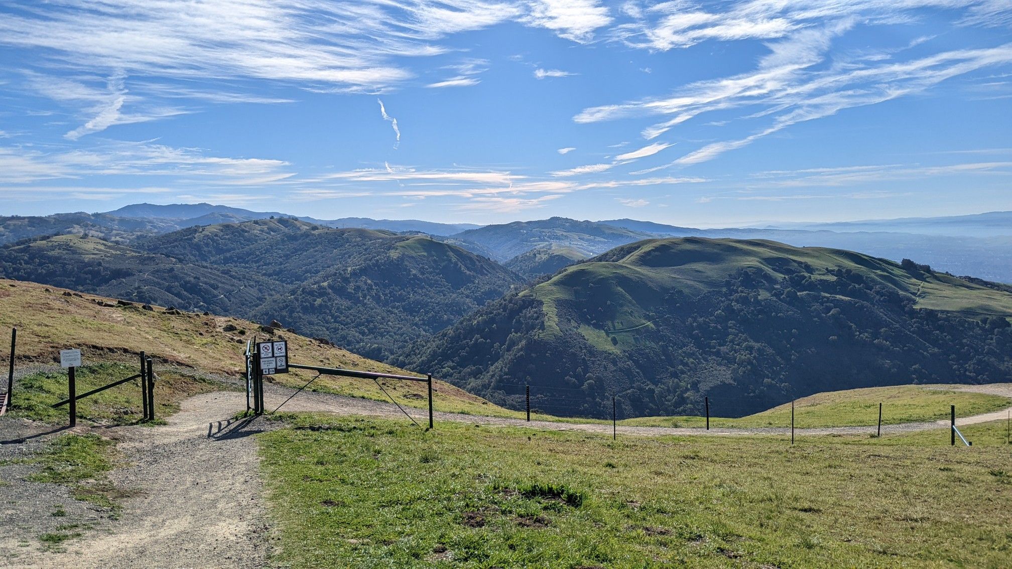 A dirt path and gate on a hilltop overlooking forested mountains under a blue sky. - Sierra Vista Viewpoint loop from Piedmont Hills High School
