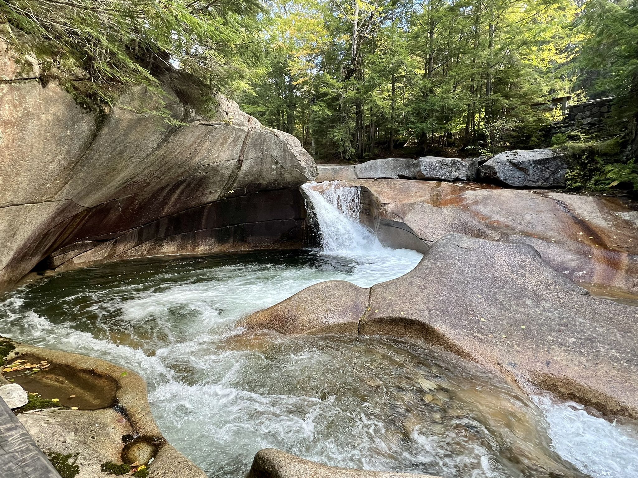 Waterfall cascades into a clear pool surrounded by smooth rocks and green trees. - Franconia Ridge Traverse