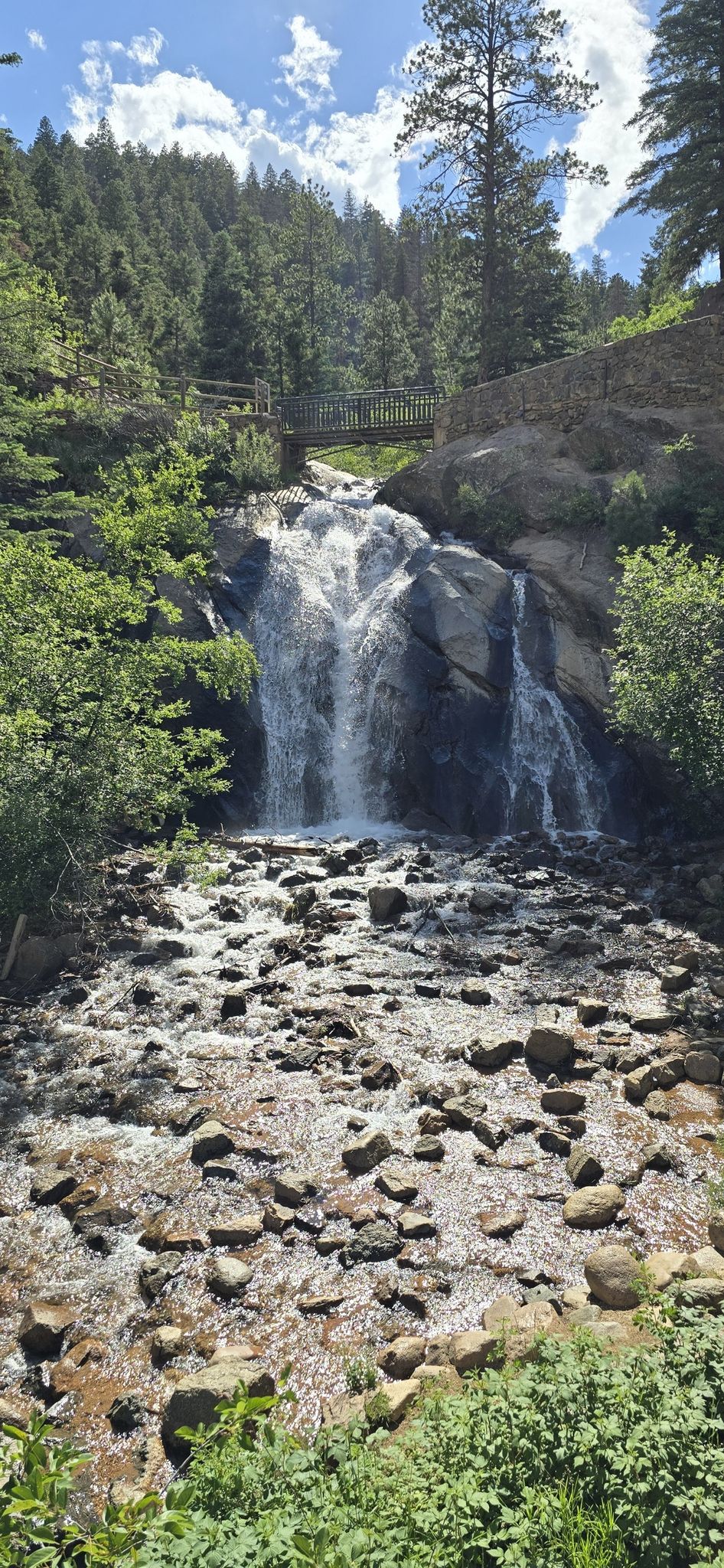 Waterfall cascading over rocks into a stream, surrounded by green trees under sunny sky. - Old Colorado City – Helen Hunt Falls loop from Colorado Springs