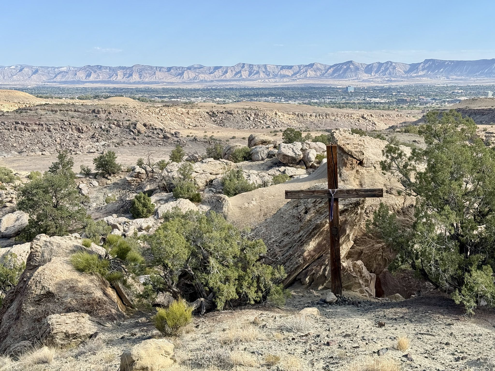 A large wooden cross stands on a rocky hill overlooking a distant valley. - Raven Ridge and Holy Cross Loop