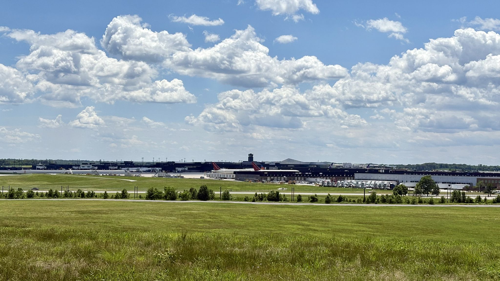 Green field with distant buildings under a bright, cloudy sky. - Tom Dixon Observation Area – Propel by James Vose loop from BWI Airport