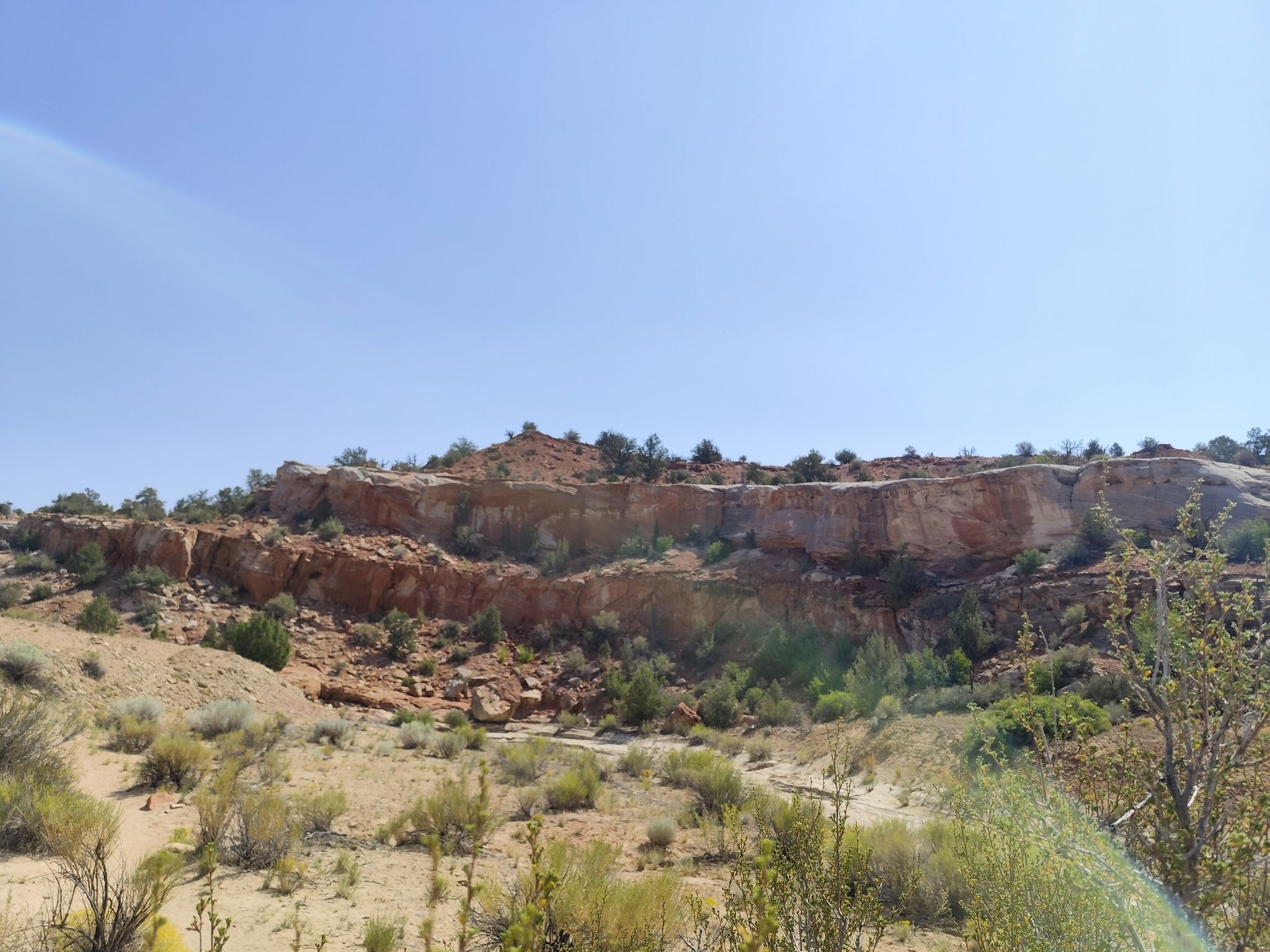 Wide view of a desert hillside with layered red rock cliffs and sparse vegetation. - Zebra and Tunnel Slot Canyons Trail
