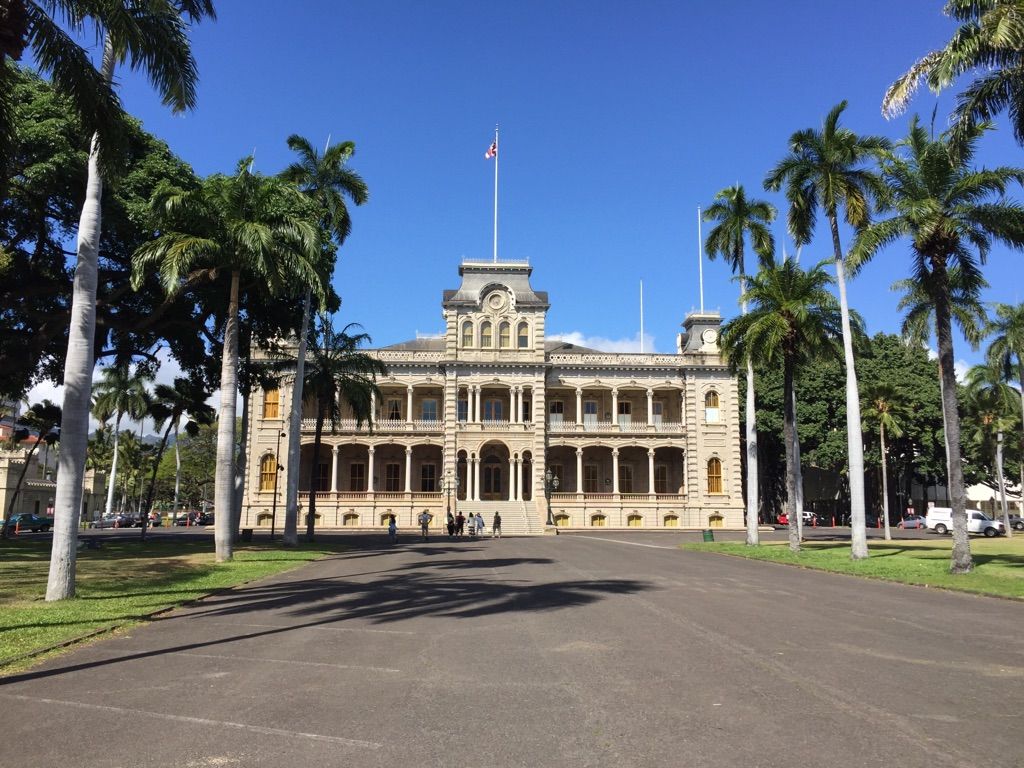 Ornate building with columns, palm trees, and a paved path on a sunny day. - Hawaii State Capitol and Palace Grounds