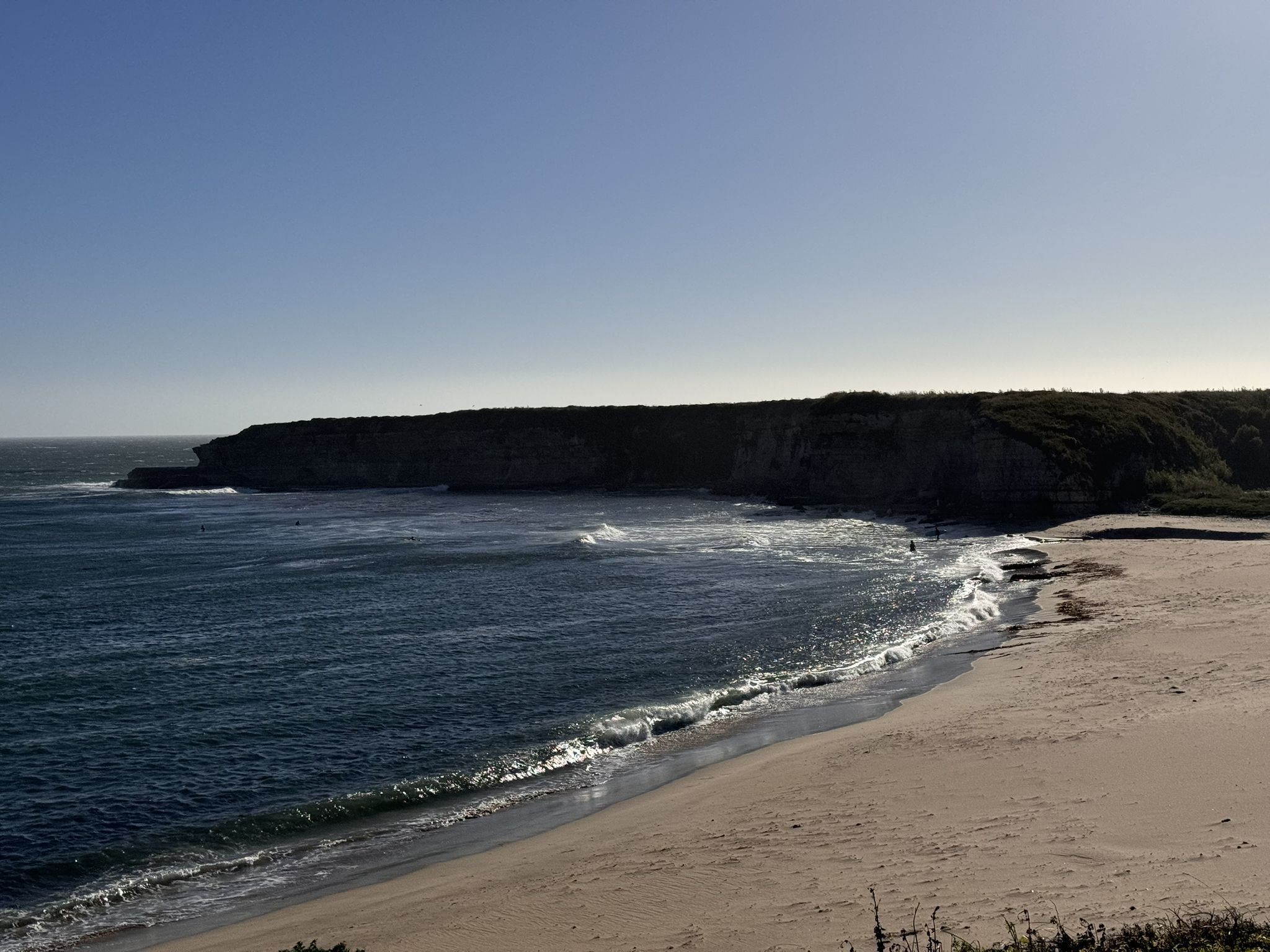 Sunny day on a wide sandy beach with dark ocean waves and rugged cliffs. - Ohlone Bluff Trail