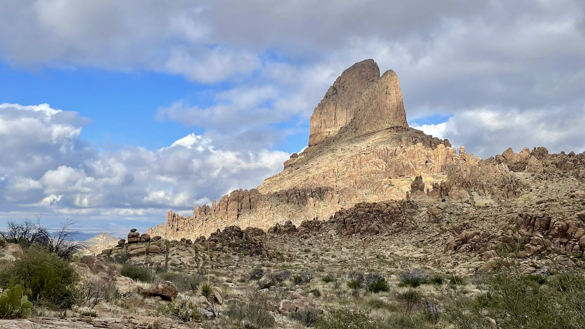 Sunny desert landscape with a large, pointed rock formation under a partly cloudy sky. - Weavers Needle Loop Trail