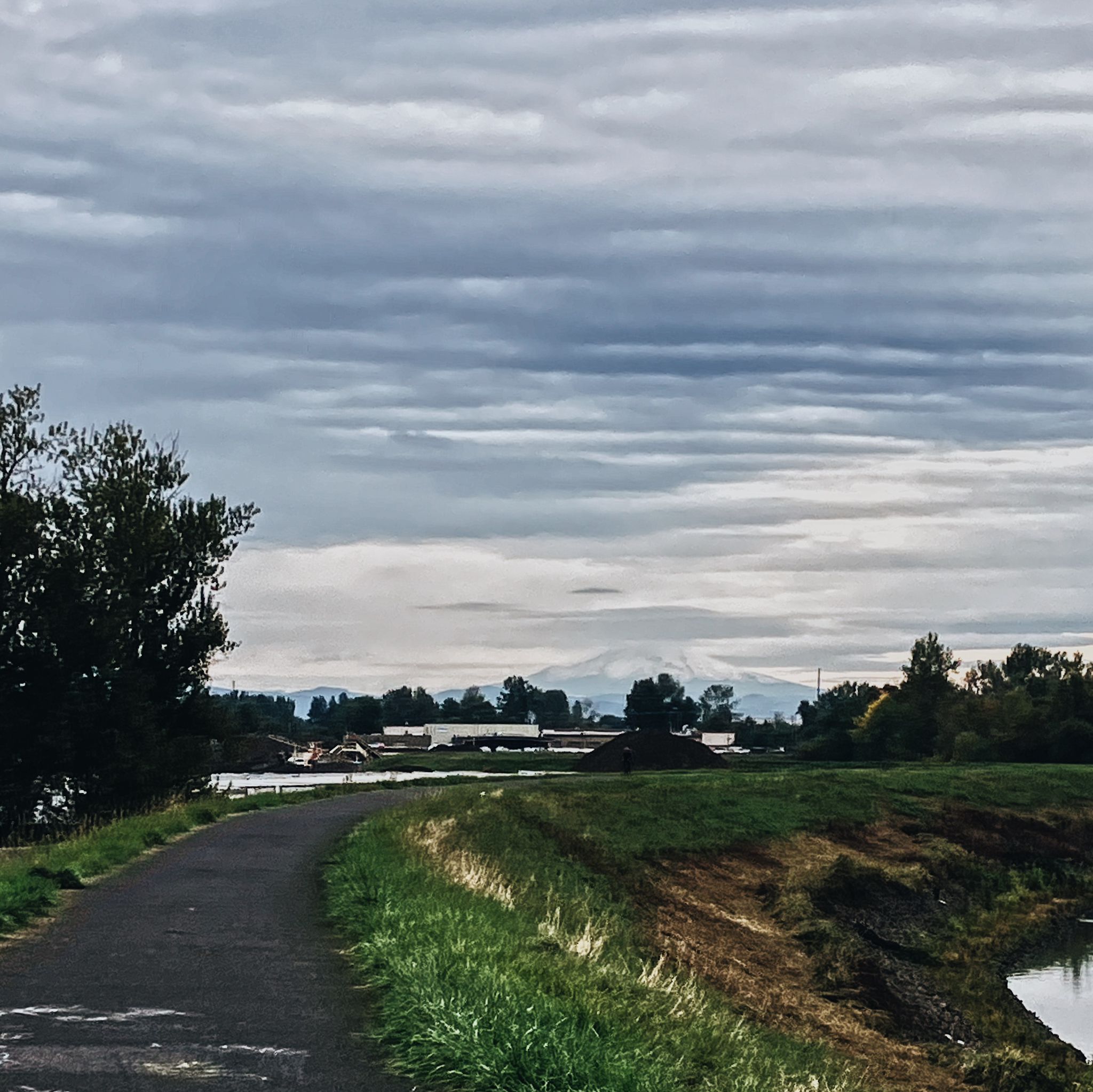 Paved path curving alongside a river with a snowy mountain under cloudy sky. - Grant Street Pier – Blumenauer Bridge loop from Hazel Dell