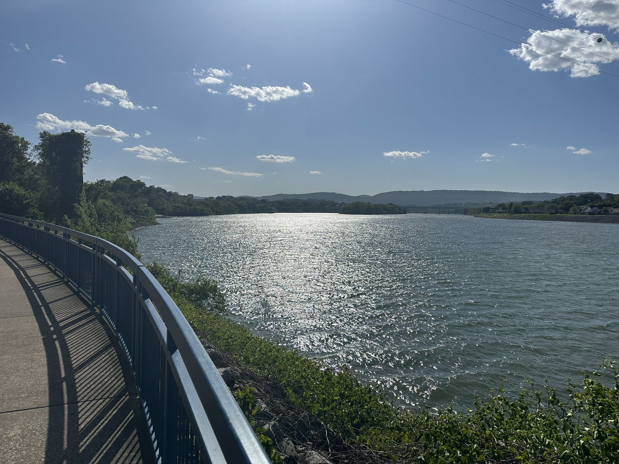 Sunny river with sparkling water next to a paved path and blue railing. - View of Lookout Mountain – Tennessee Riverwalk loop from East Chattanooga