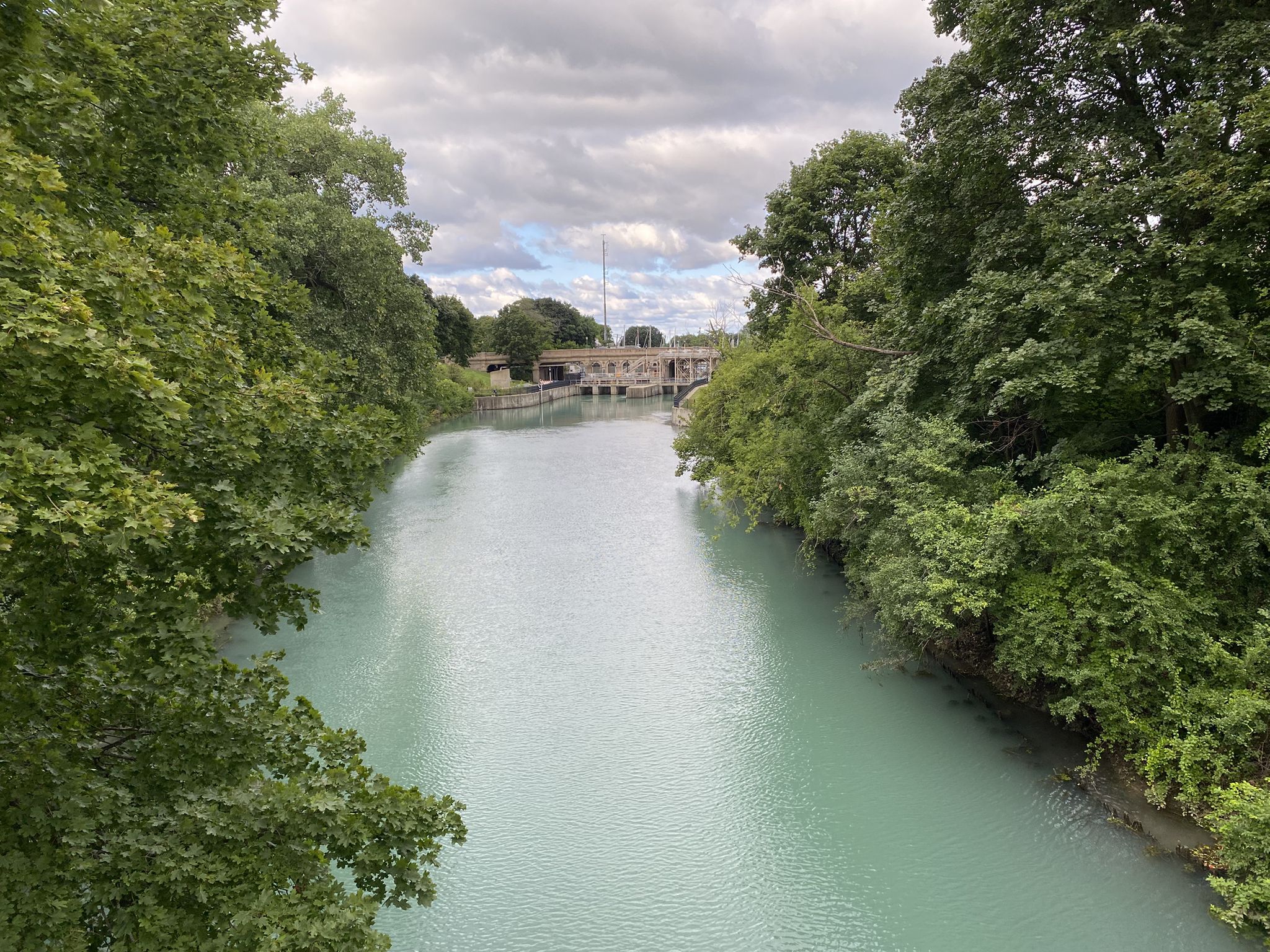 A wide, light blue river flows between lush green trees under a cloudy sky. - Baha'i Temple loop via North Shore Channel Trail