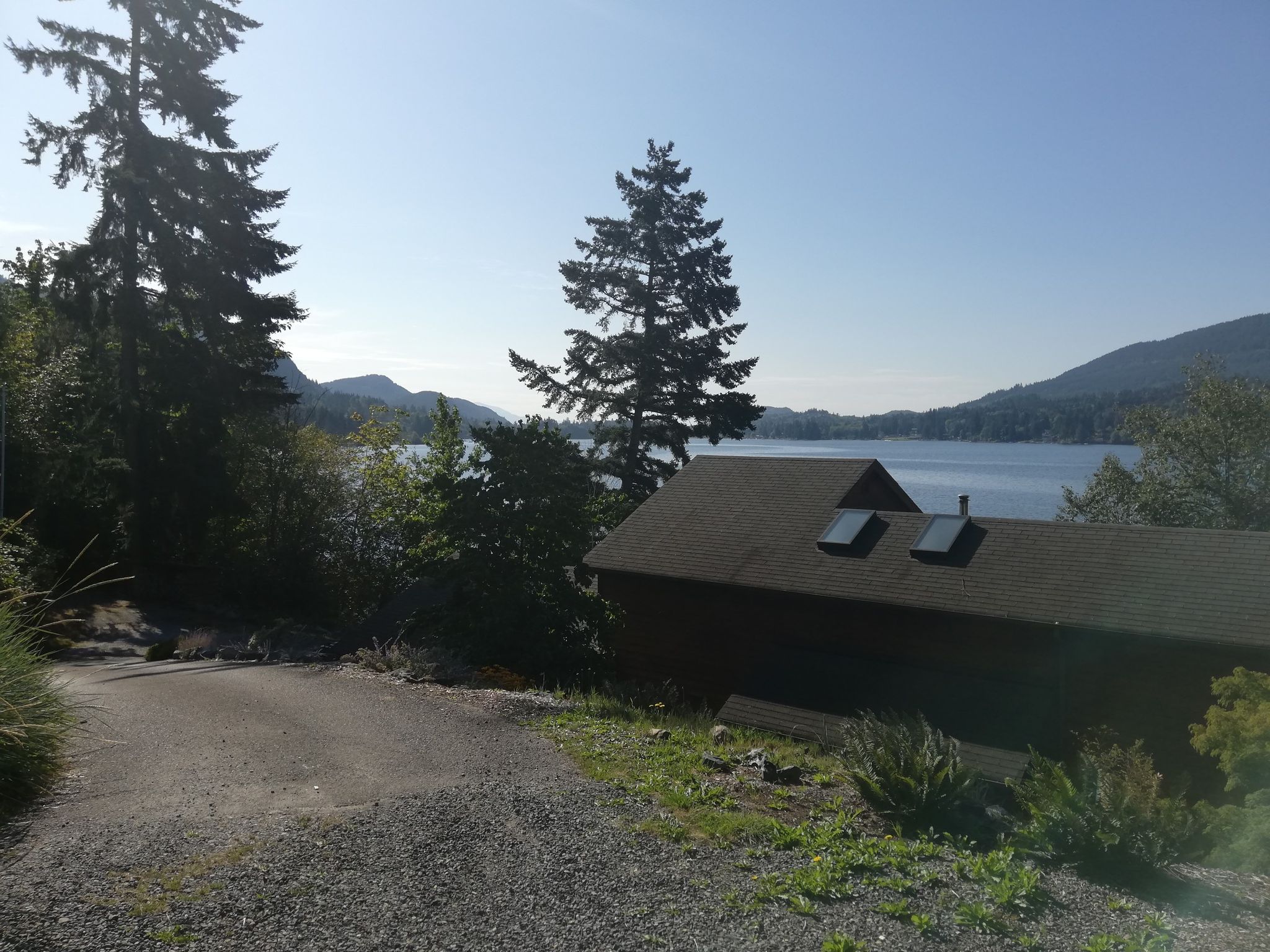 A house overlooks a large lake and distant mountains on a sunny day. - Lake Samish – Lake Samish loop from Edison