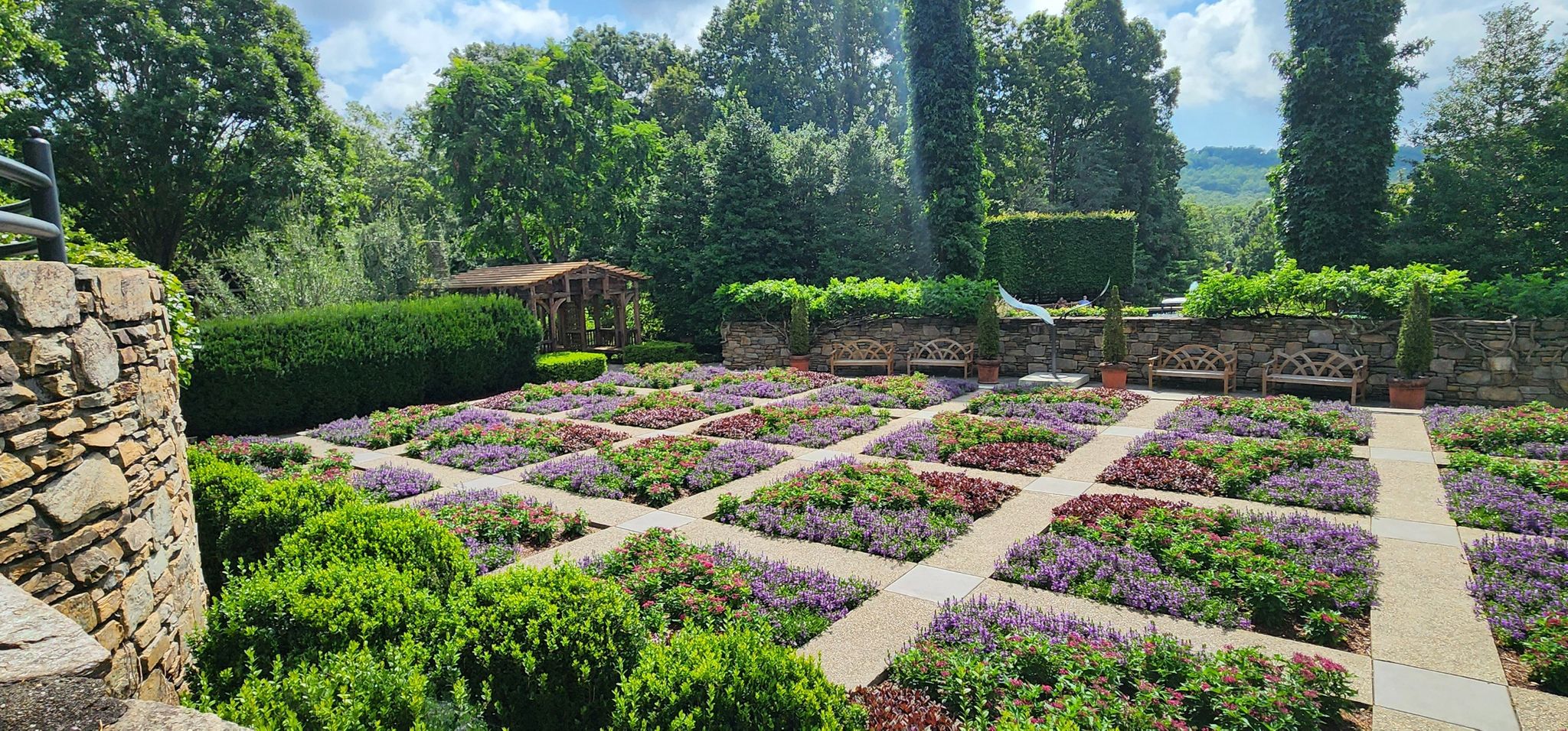 Formal garden with square flower beds, stone walls, and lush trees under cloudy sky. - Natural Garden, Bent Creek and Carolina Mountain Loop