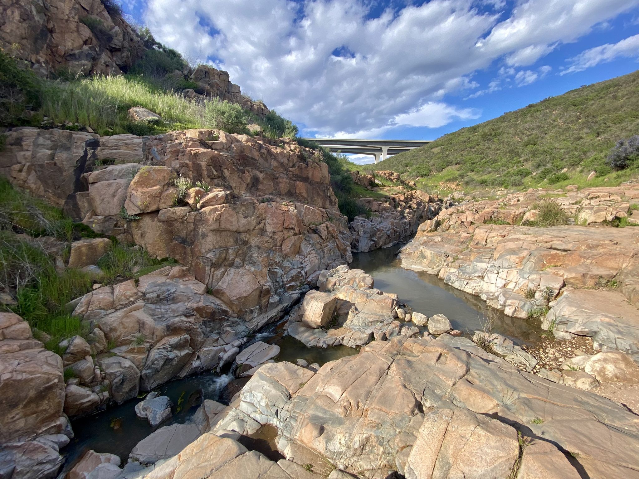 Rocky canyon with a stream, under a bridge and cloudy sky. - Oak Canyon Trail