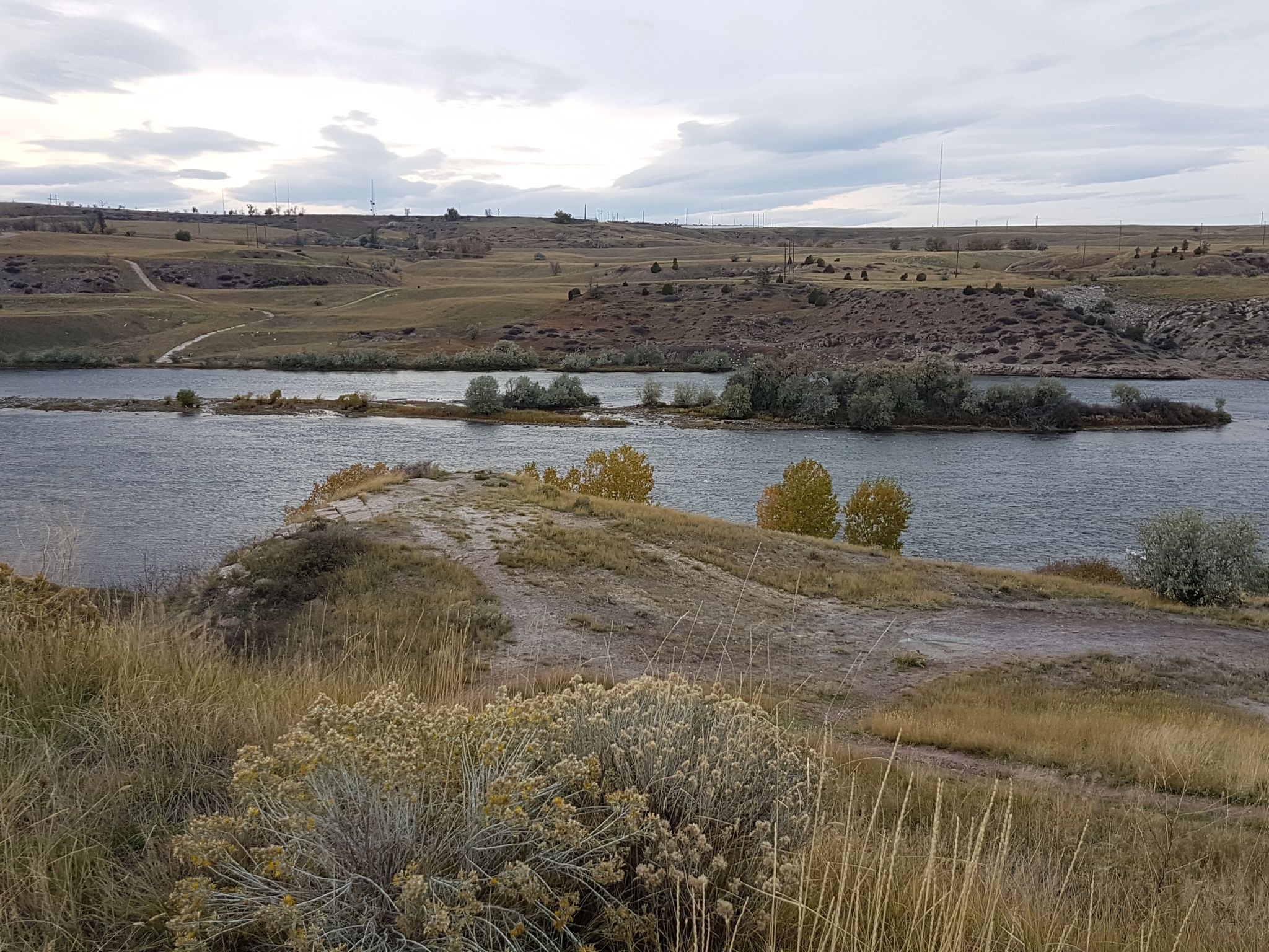 Wide river flowing through dry, grassy landscape under an overcast sky. - River's Edge Trail