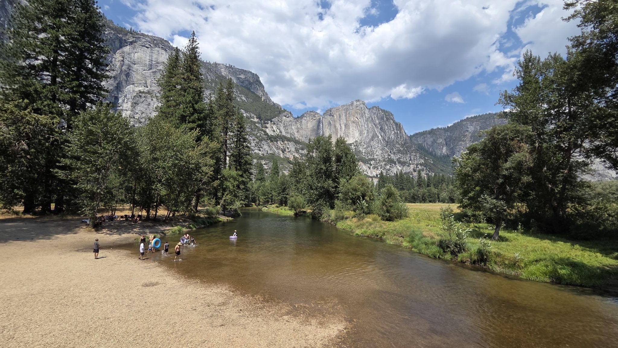 A group of people wade in a wide river with towering rocky mountains. - View of Yosemite Valley – Lower Yosemite Falls Viewpoint loop from Ahwahnee Hotel