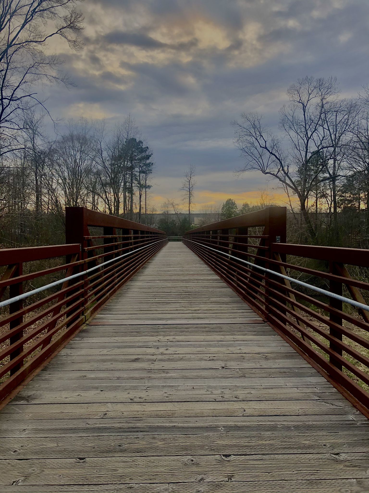 A long metal bridge extends into the distance under a cloudy sunset sky. - Anderson Point Park – Crabtree Park loop from Randleigh Farm