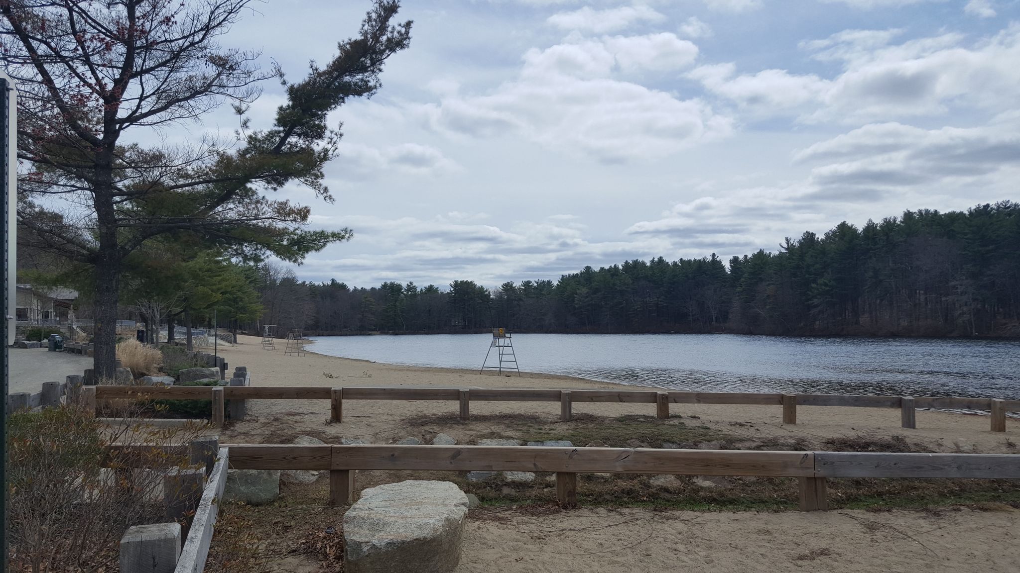 A lake with a sandy beach and lifeguard stand under a cloudy sky. - Houghton's Pond Recreation Area