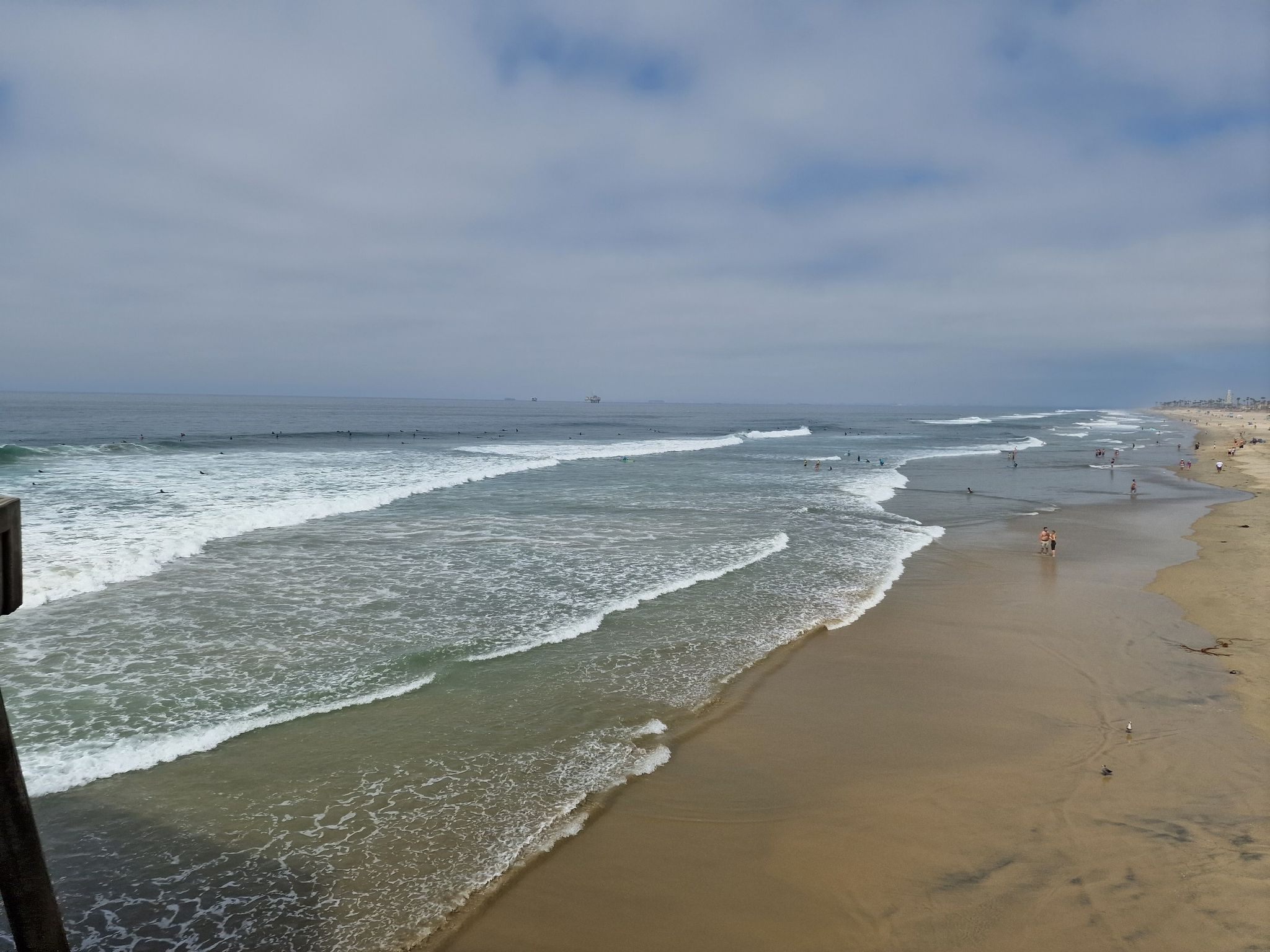 Ocean waves breaking on a sandy beach with distant people under cloudy sky. - Huntington Beach Pier – Huntington City Beach loop from Huntington State Beach