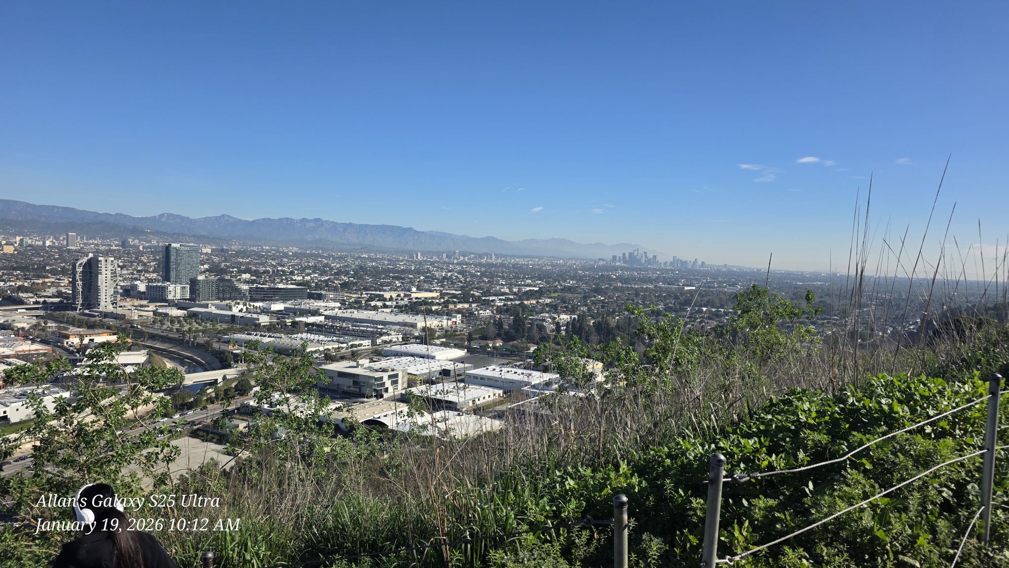 A panoramic city view from a brushy hillside with a wire fence on a clear day. - Baldwin Hills – View of Beverly Hills loop from NPR West