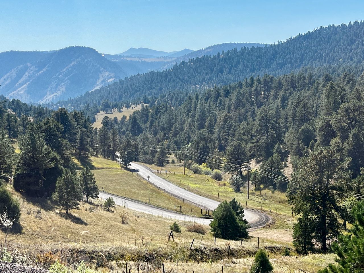 A winding road cuts through a dense pine forest in sunny mountains. - South Grapevine Road – Dinosaur Bone Bend loop from Idledale