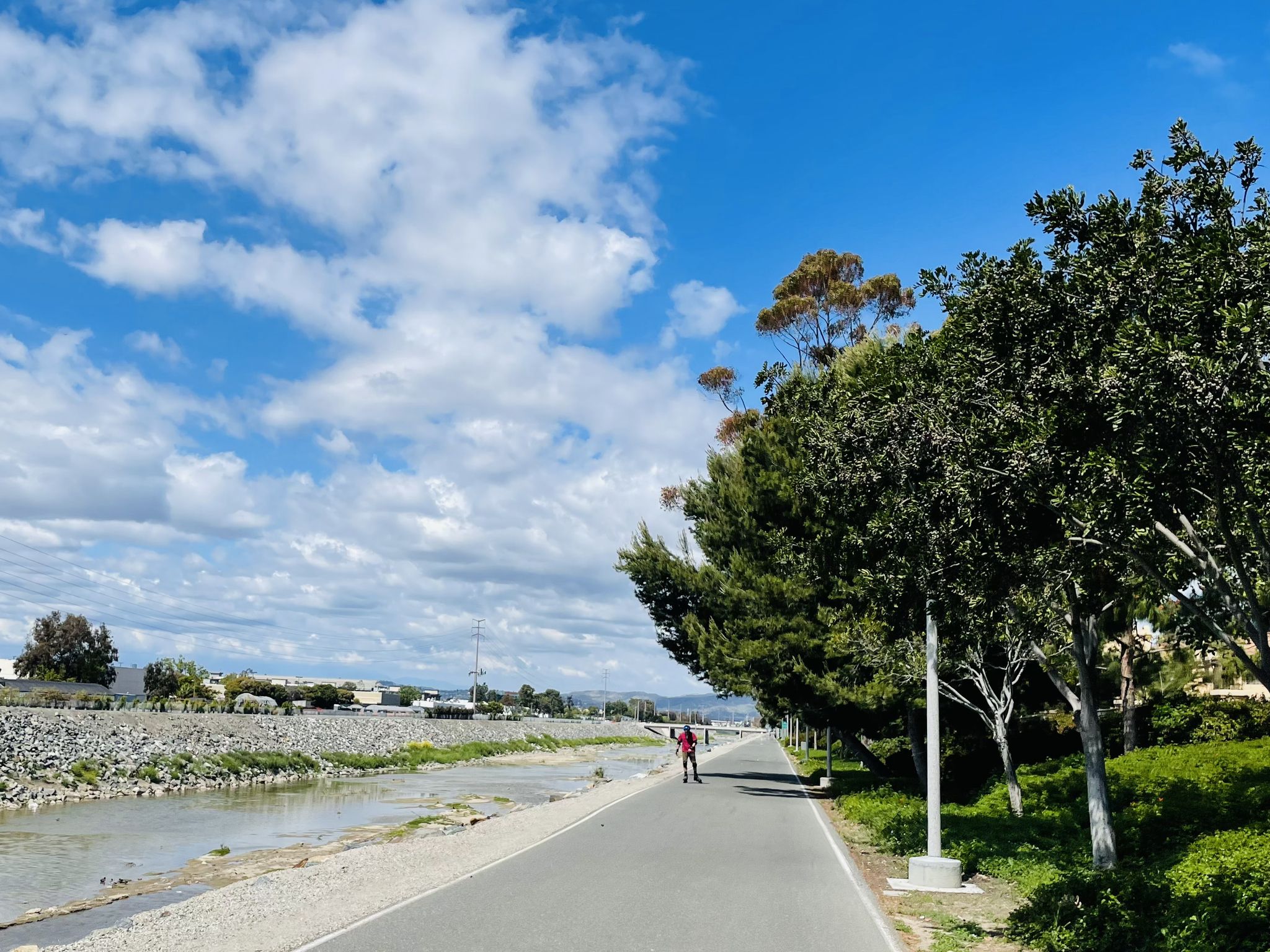 Paved path alongside a river with lush trees and a person walking. - San Diego Creek Trail – San Diego Creek loop from Northwood