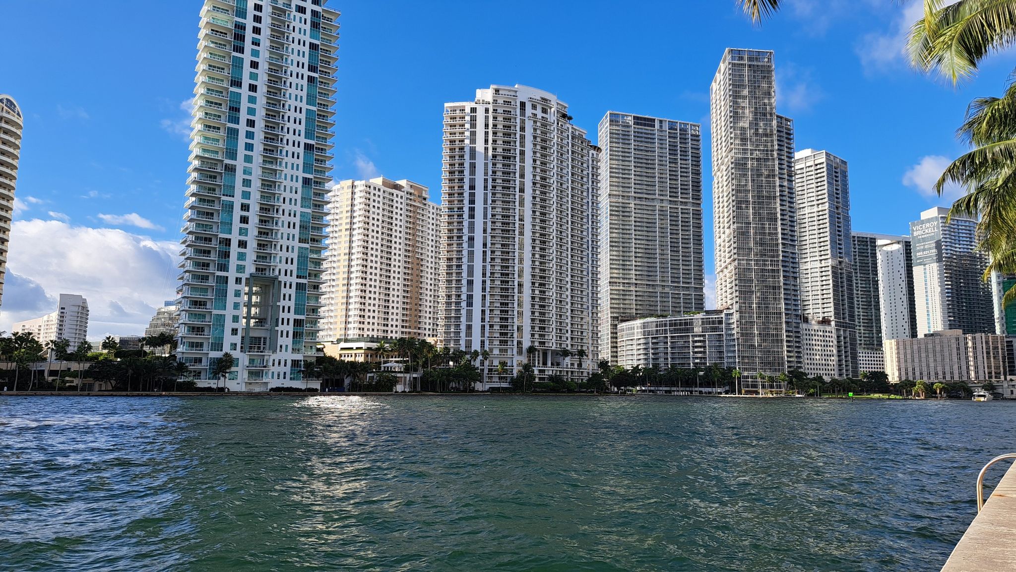 Tall buildings line a sunny waterfront with blue skies and clouds. - Miami Baywalk and Riverwalk