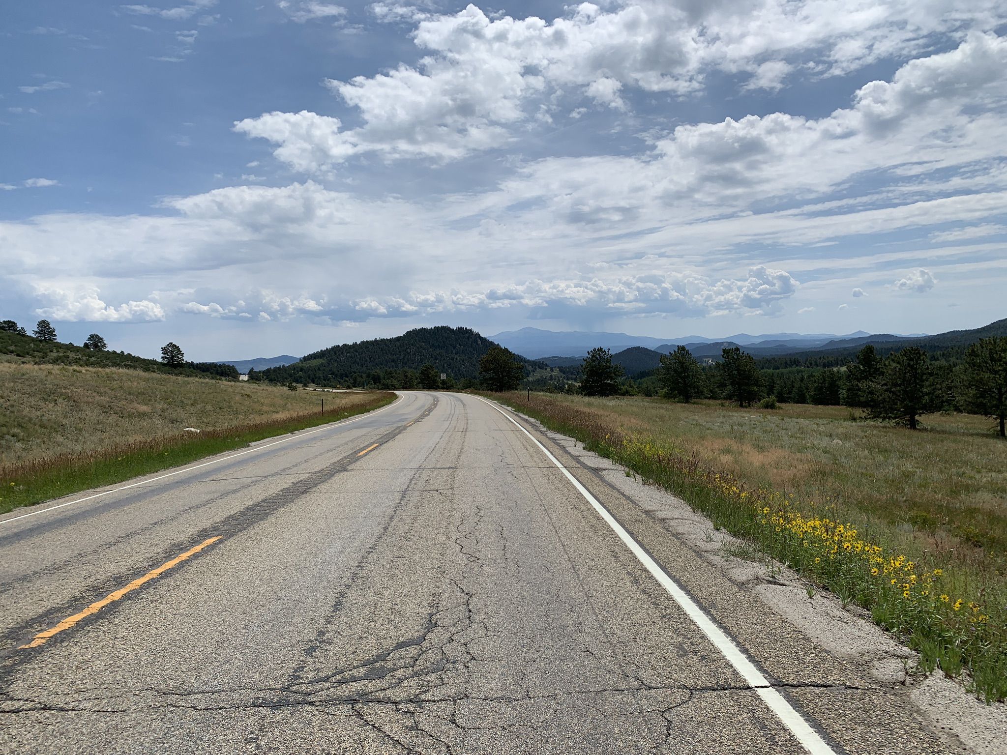 A winding paved road through grassy hills under a partly cloudy sky. - Lake George
