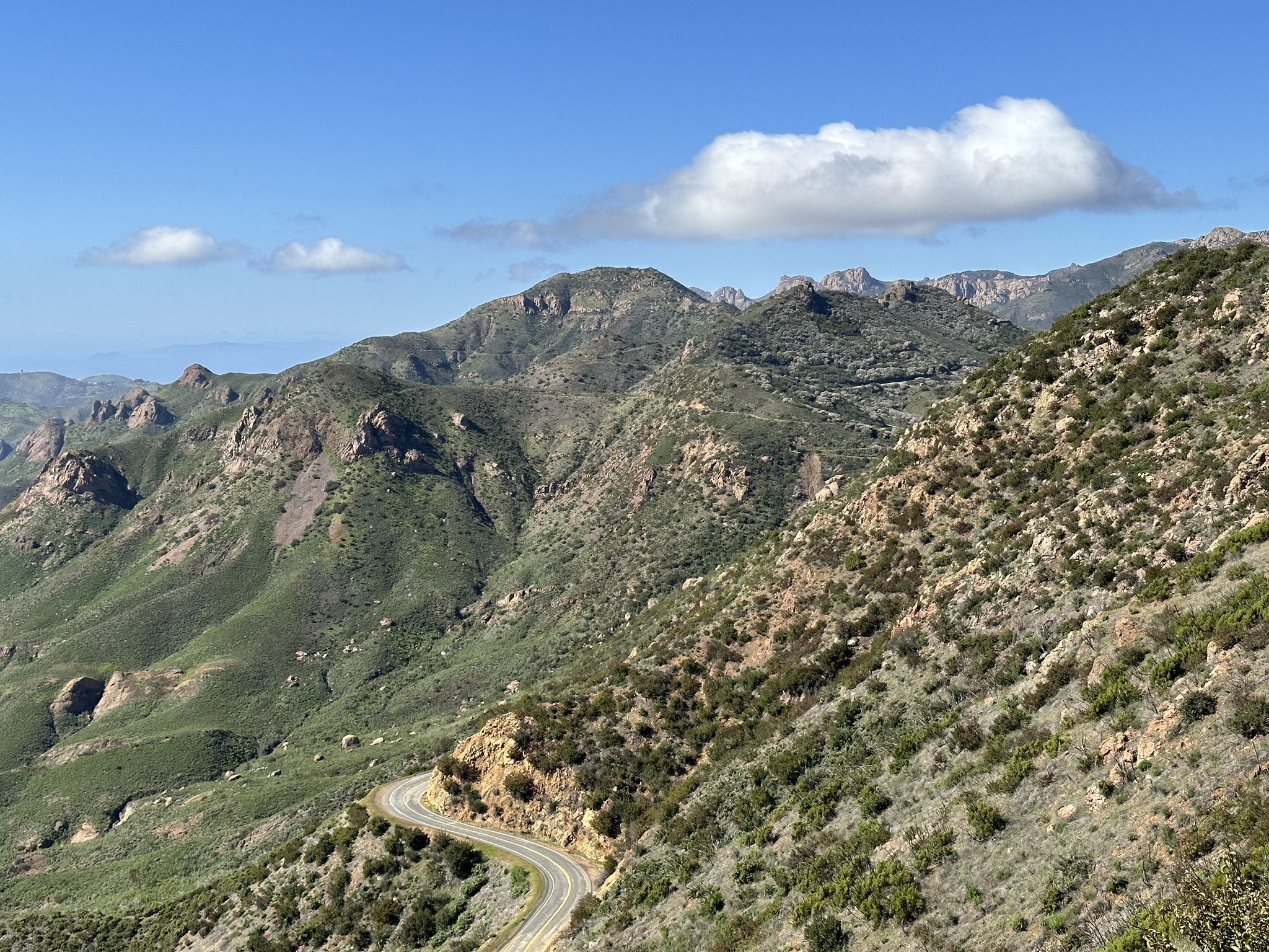 Winding road through green, rocky mountains under a blue sky with clouds. - Backbone Trail: Newton Canyon to Triunfo Pass