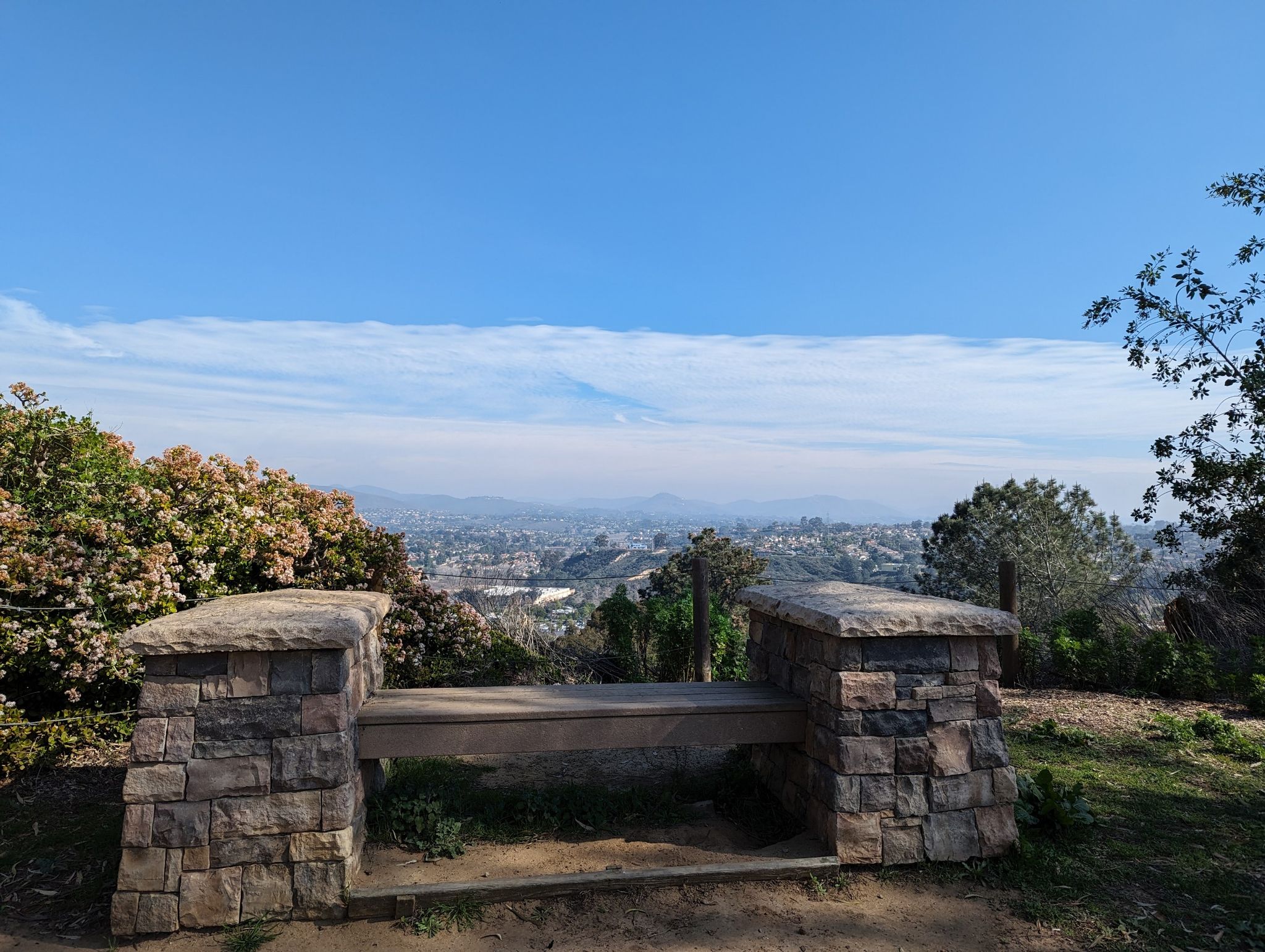 Stone bench overlooks a hazy distant city under a blue sky. - Encinitas Ranch Trail