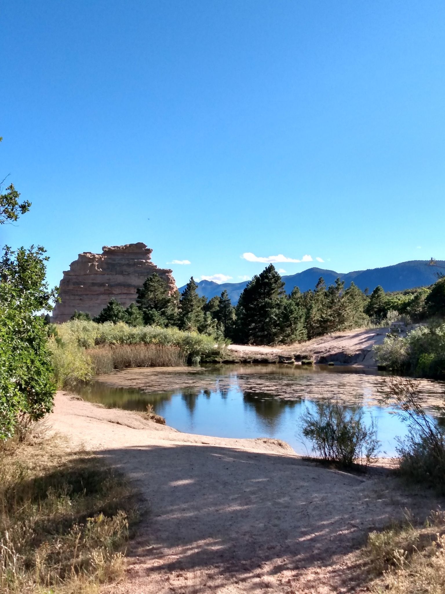 Sunny pond reflecting blue sky, with large rock formations and distant mountains. - Monument Rock loop from Monument Rock