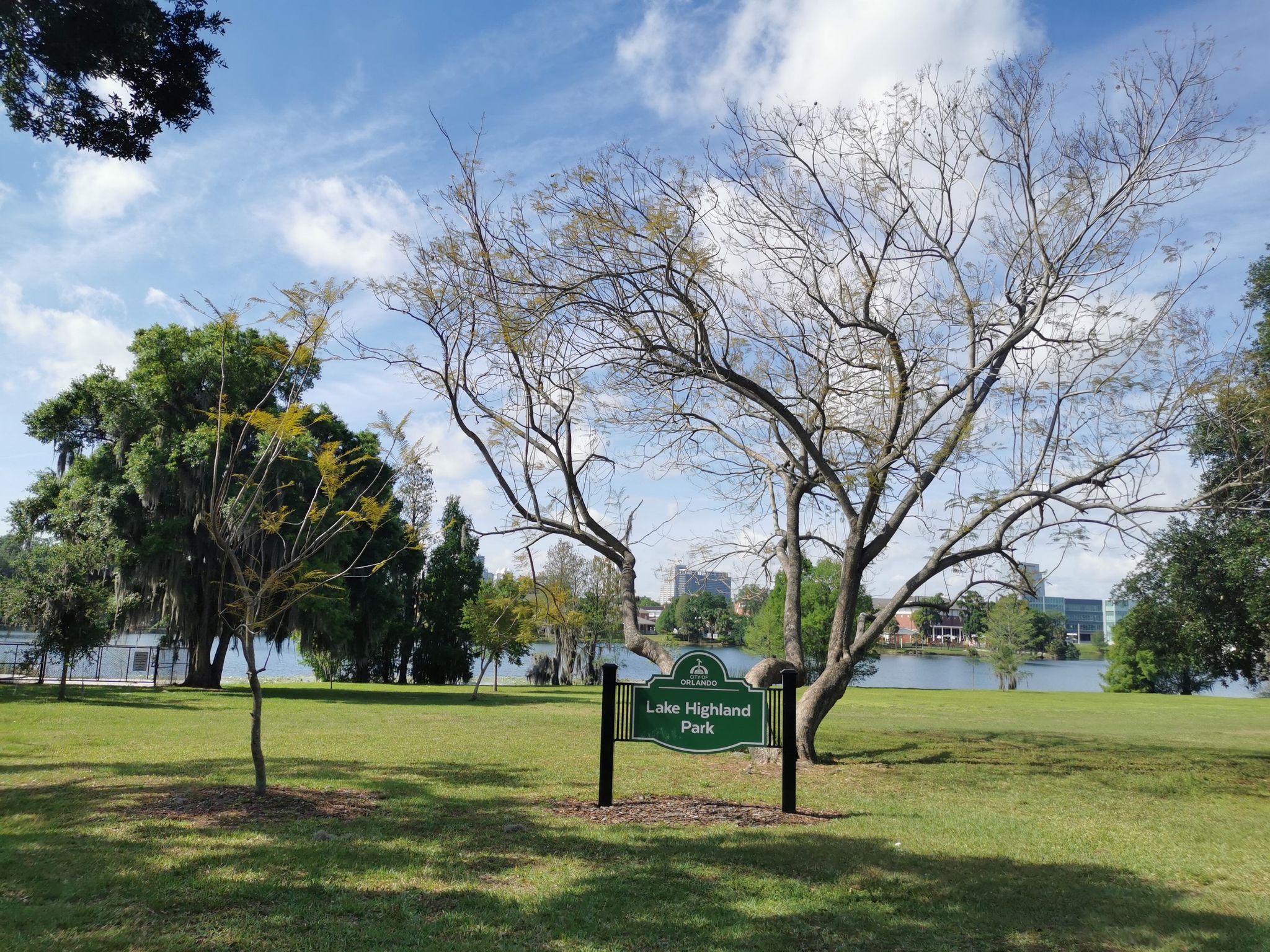 Grassy park with large trees, a sign, and a lake under a cloudy sky. - Lake Davis to Lake Highland Park loop