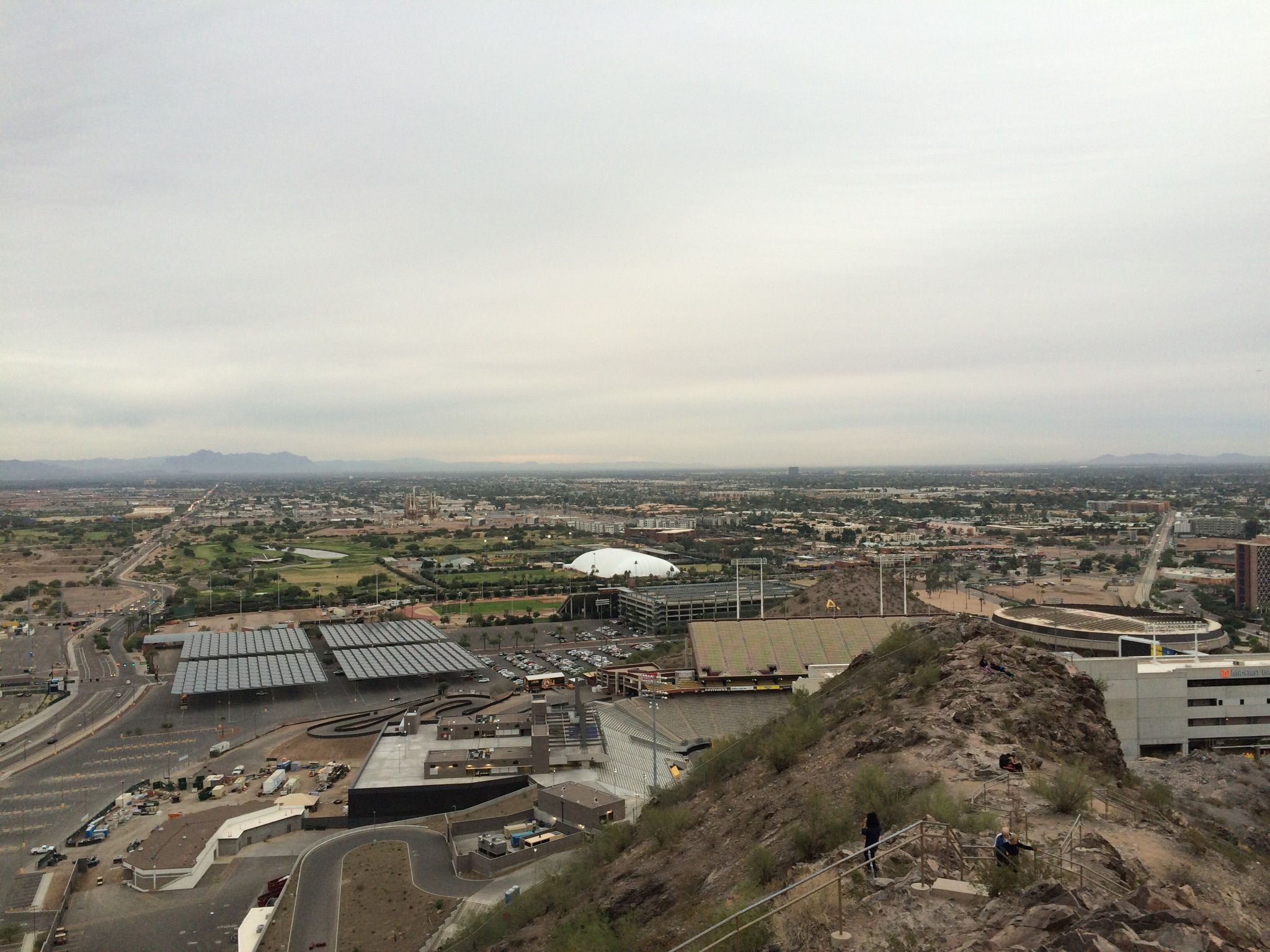 Overcast daytime view of a city from a rocky hill, with distant mountains. - Leonard Monti Trail