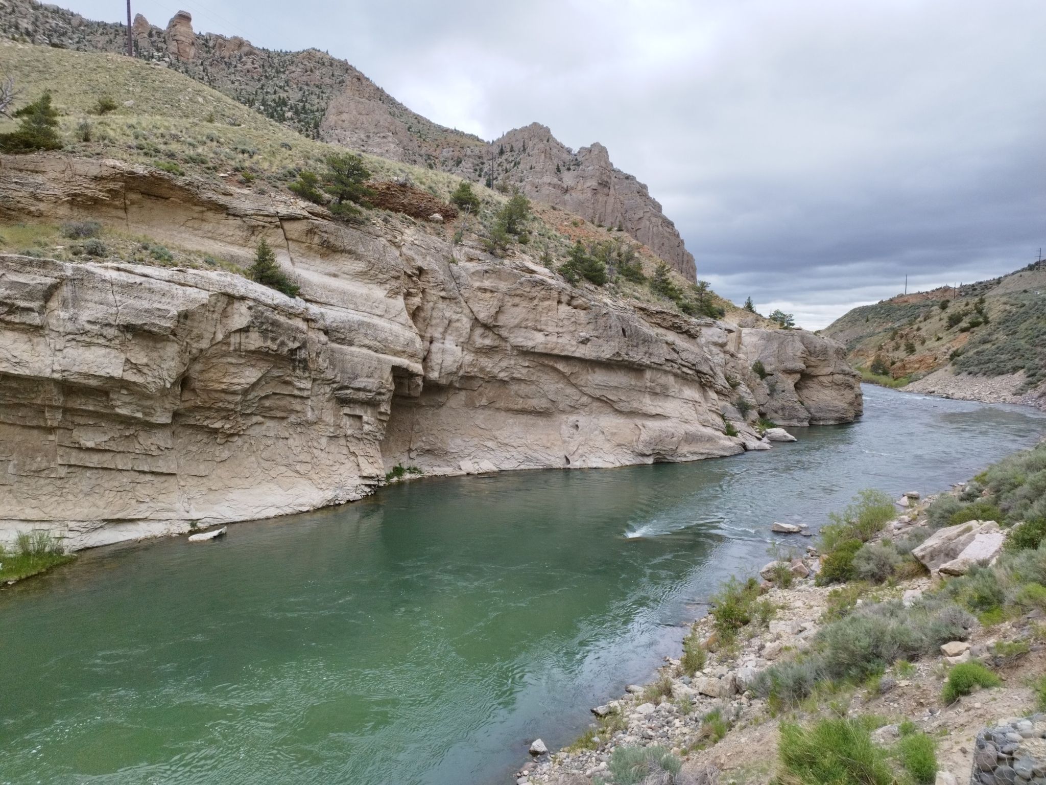 River flows through a deep rocky canyon under a cloudy sky. - Buffalo Bill Dam via Hayden Arch Bridge